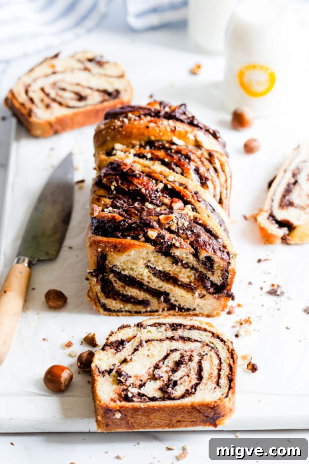 A close-up, 45-degree angle view of a golden-brown Nutella babka loaf with several slices cut off, revealing irresistible chocolate hazelnut swirls.