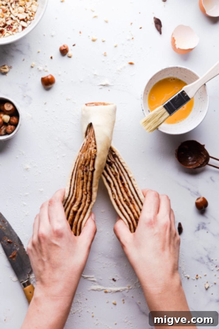 Overhead view of a person expertly twisting two chocolate-filled babka dough strands together to form a beautiful braid.