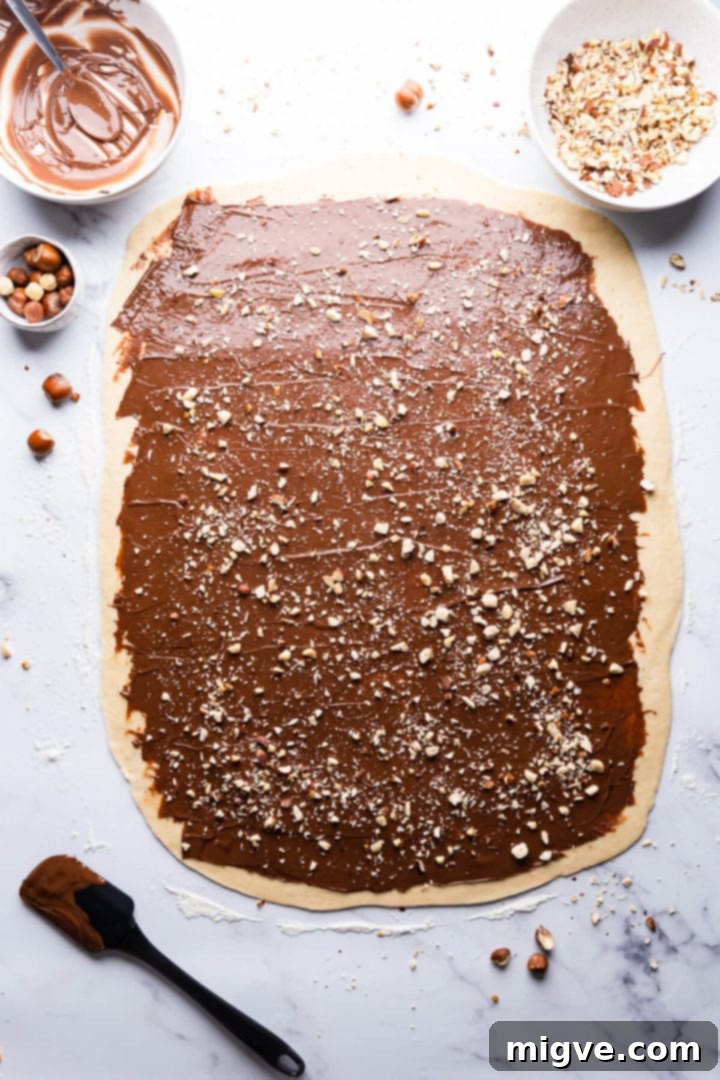 Overhead view of babka dough generously topped with a layer of Nutella and scattered chopped hazelnuts.