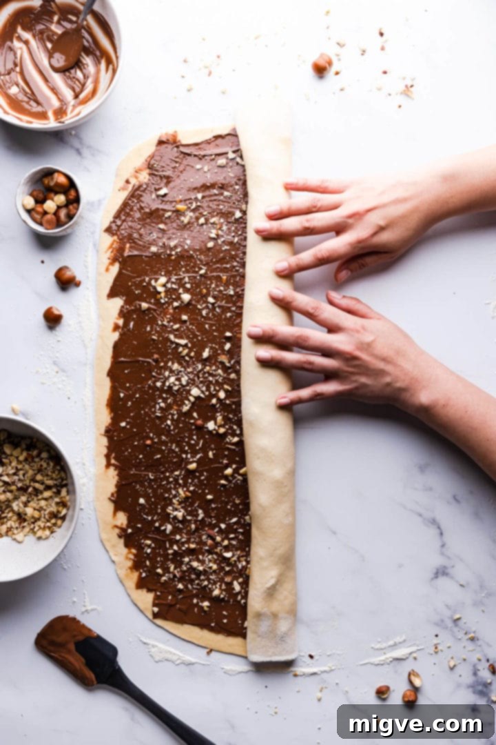 Overhead view of a person carefully rolling the babka dough, filled with Nutella and hazelnuts, into a tight log.
