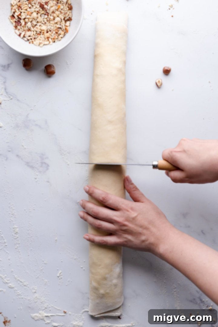 Overhead view of the rolled babka dough log being precisely sliced in half with a sharp knife.