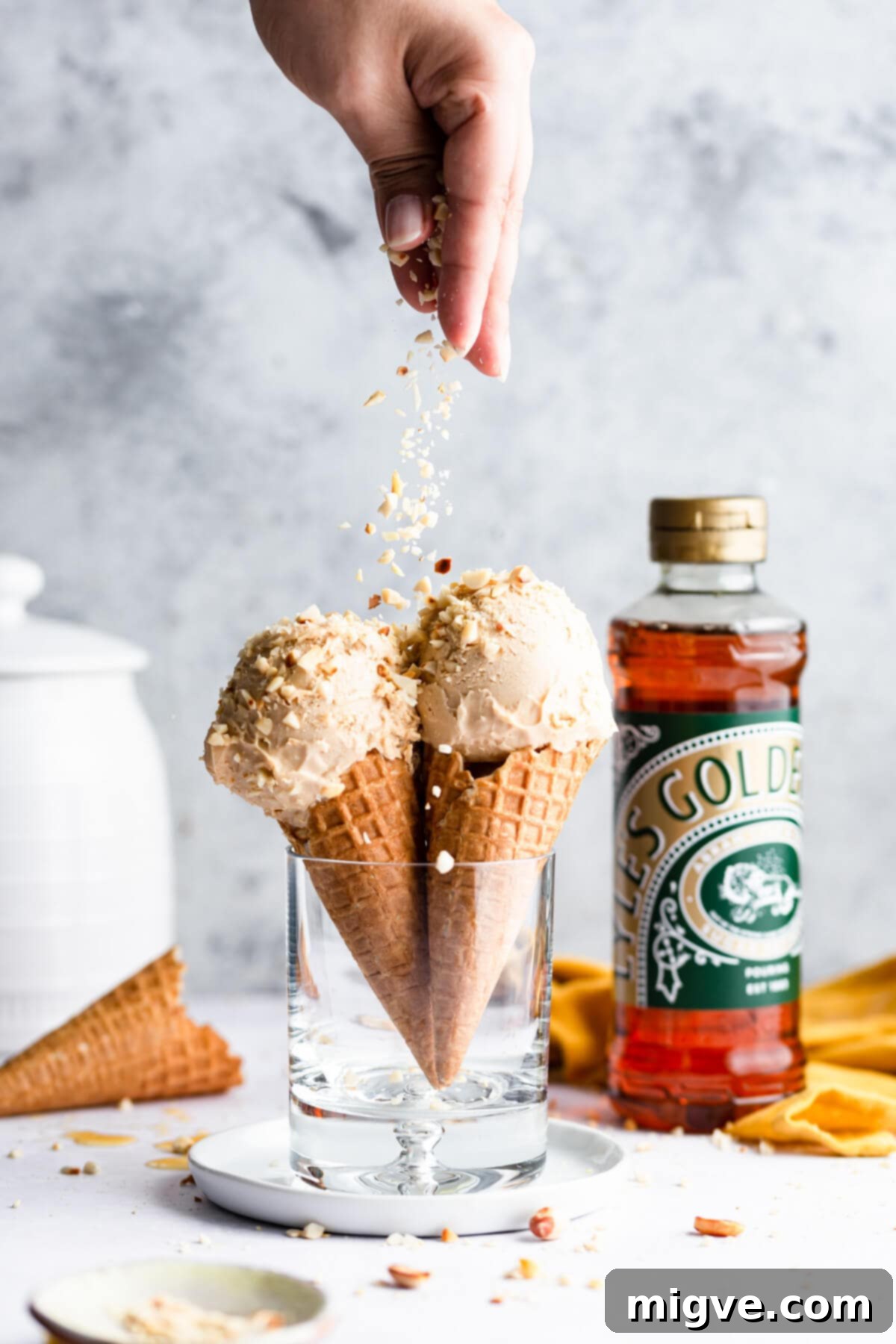 side view of a hand sprinkling chopped peanuts on top of ice cream