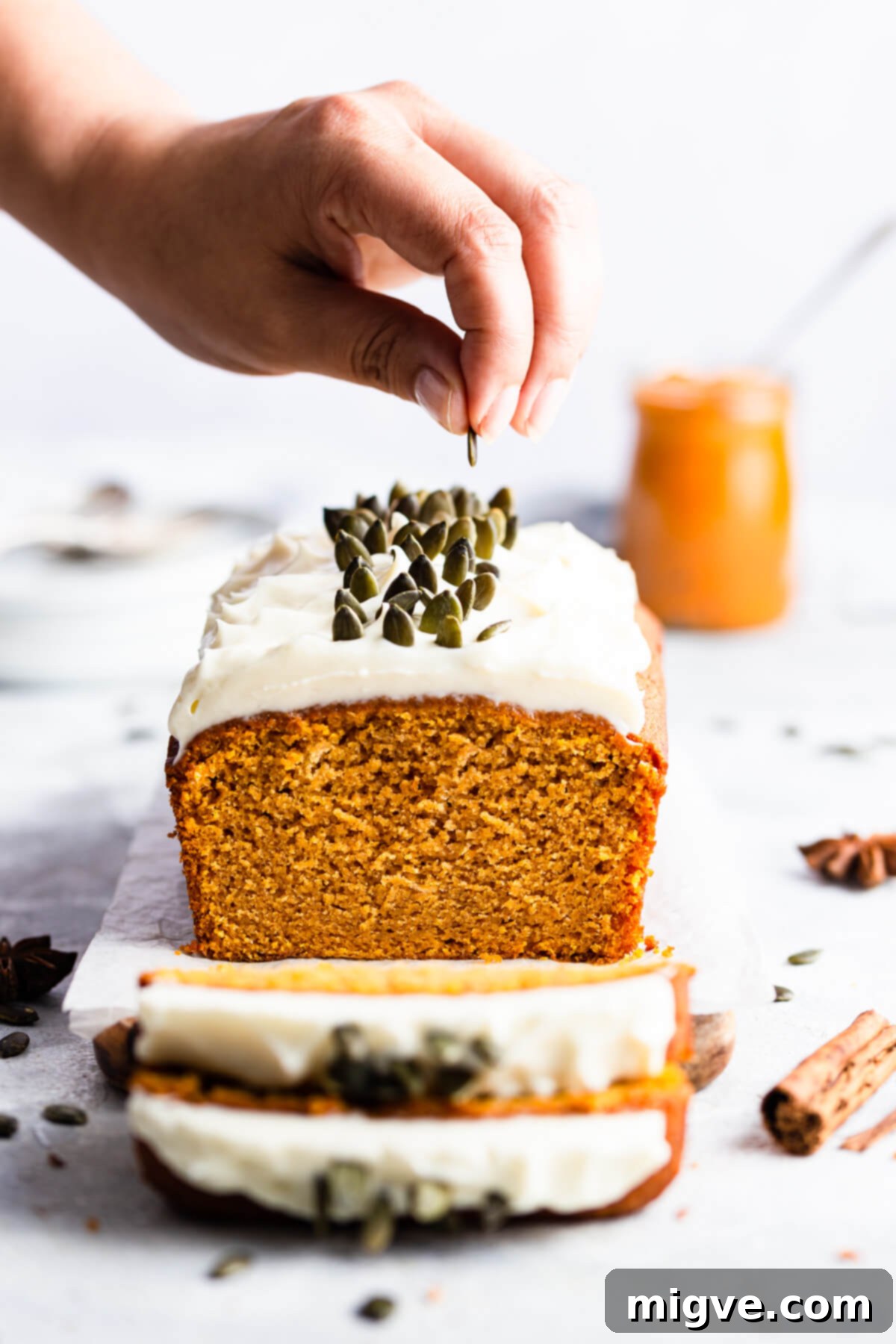 Straight ahead shot of a freshly baked pumpkin loaf cake being topped with pumpkin seeds and creamy frosting.