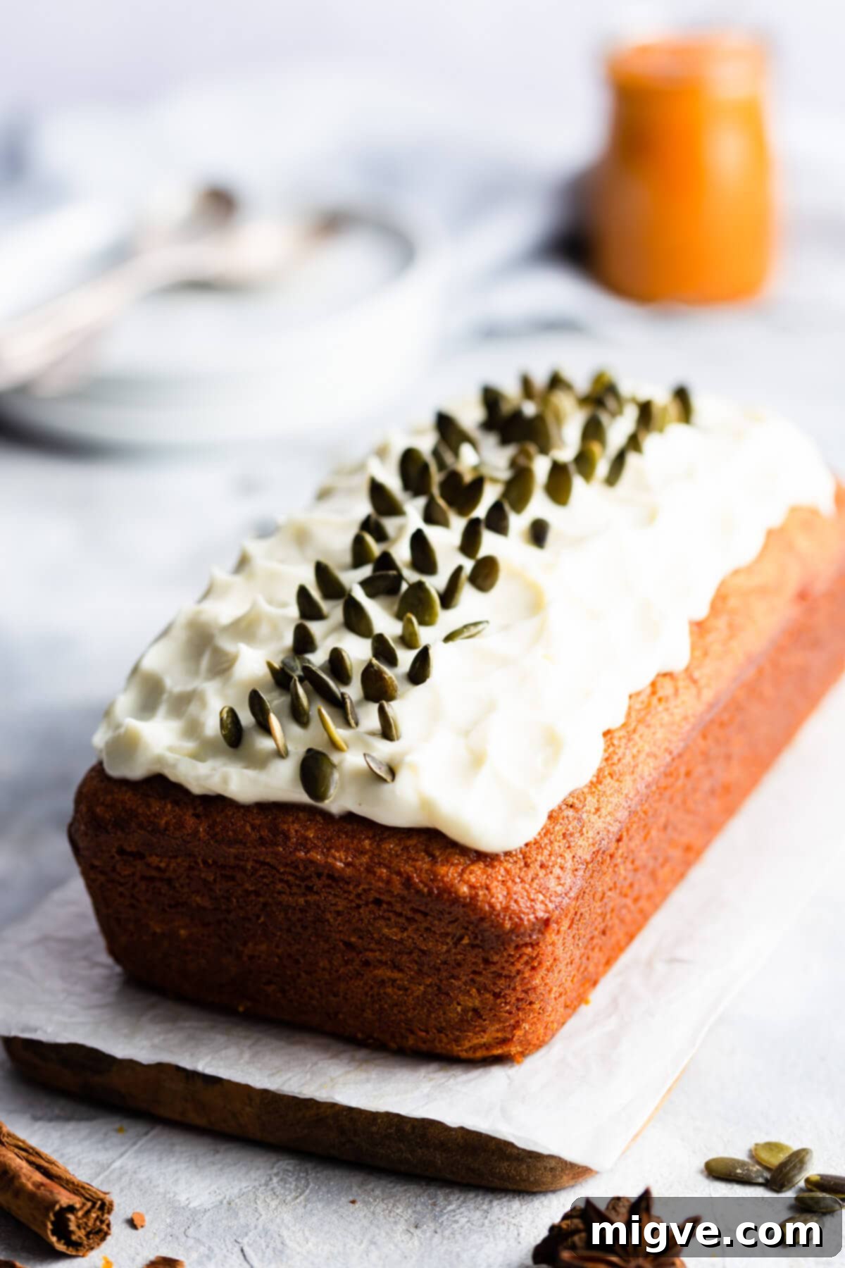 Close-up side view of a pumpkin loaf cake generously topped with cream cheese frosting and sprinkled with pumpkin seeds.