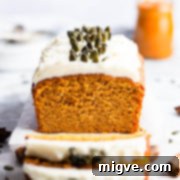 Straight ahead close-up shot of pumpkin loaf cake topped with cream cheese and pumpkin seeds.