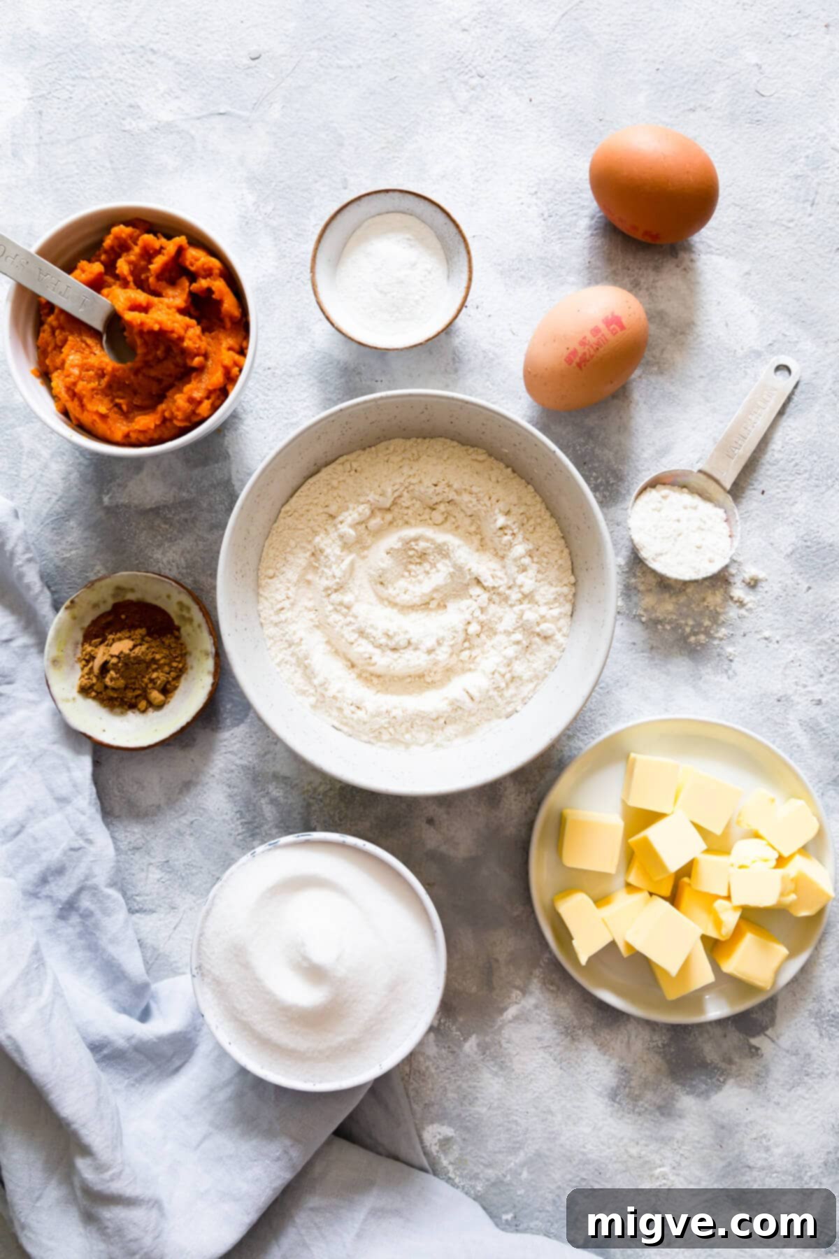 Top-down view of various bowls containing ingredients for pumpkin bread, including flour, sugar, eggs, and pumpkin puree.