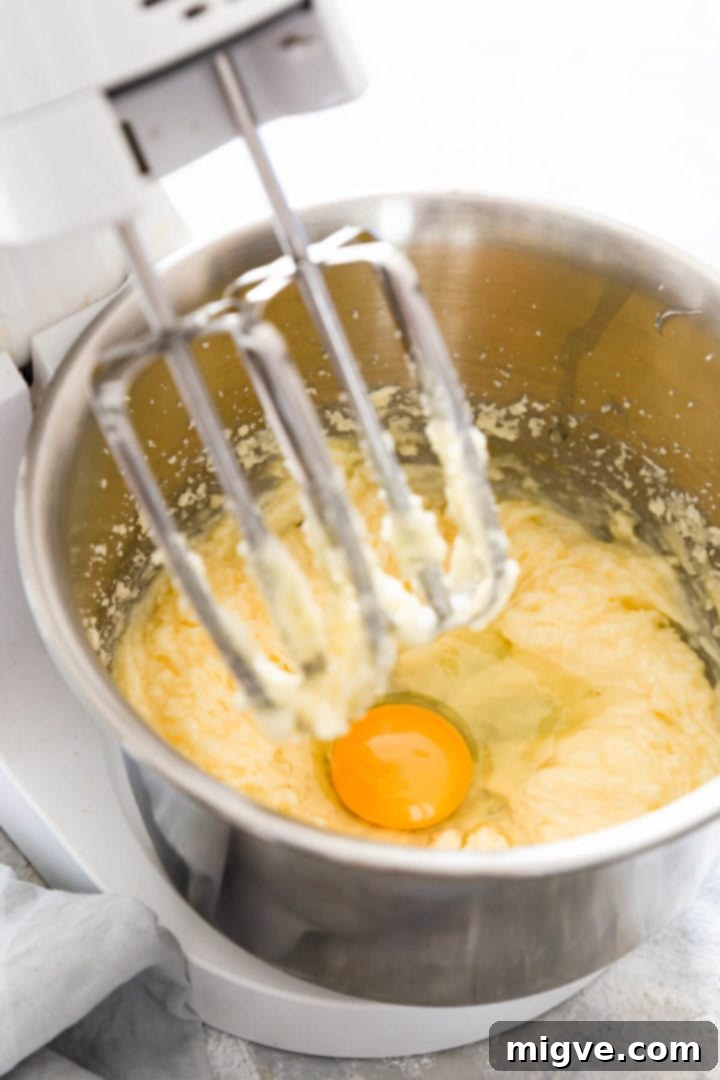 A 45-degree angle view of a mixing bowl containing creamed butter and sugar, with an egg being added.