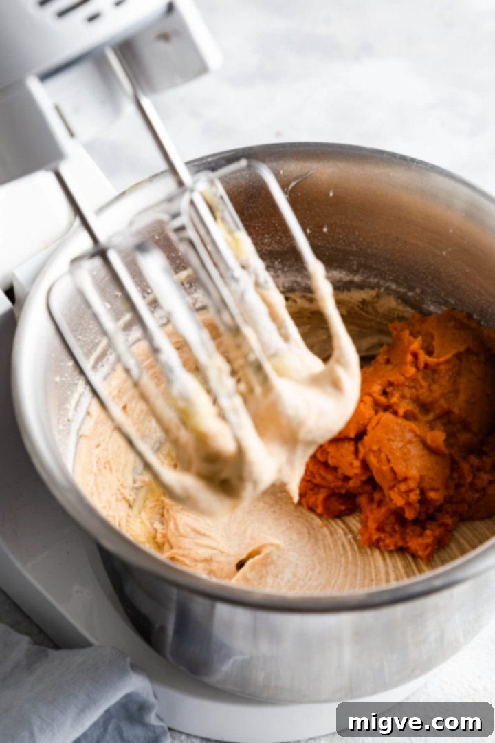 Side angle view of a mixing bowl with pumpkin puree being added to the cake batter.