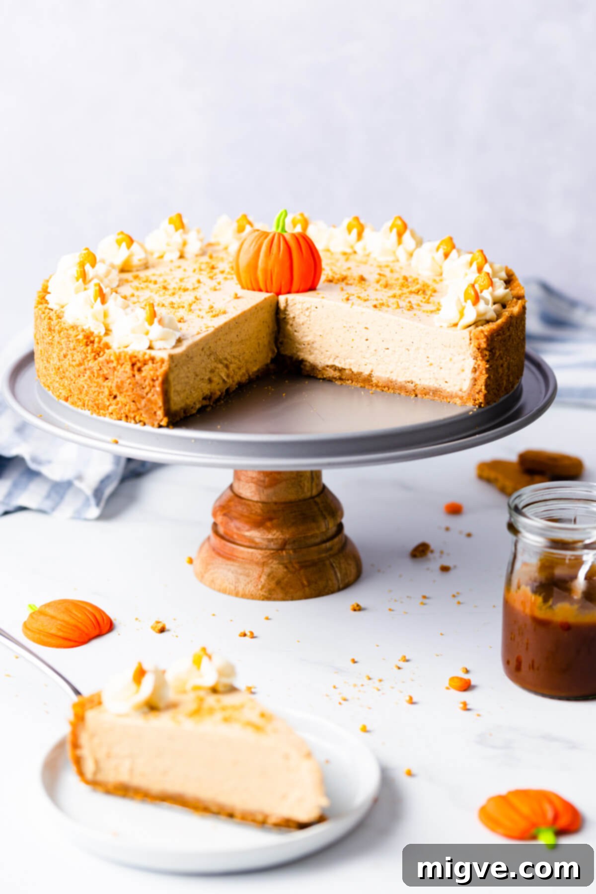 straight ahead angle of a no bake pumpkin cheesecake on a small cake stand with couple of pieces cut out