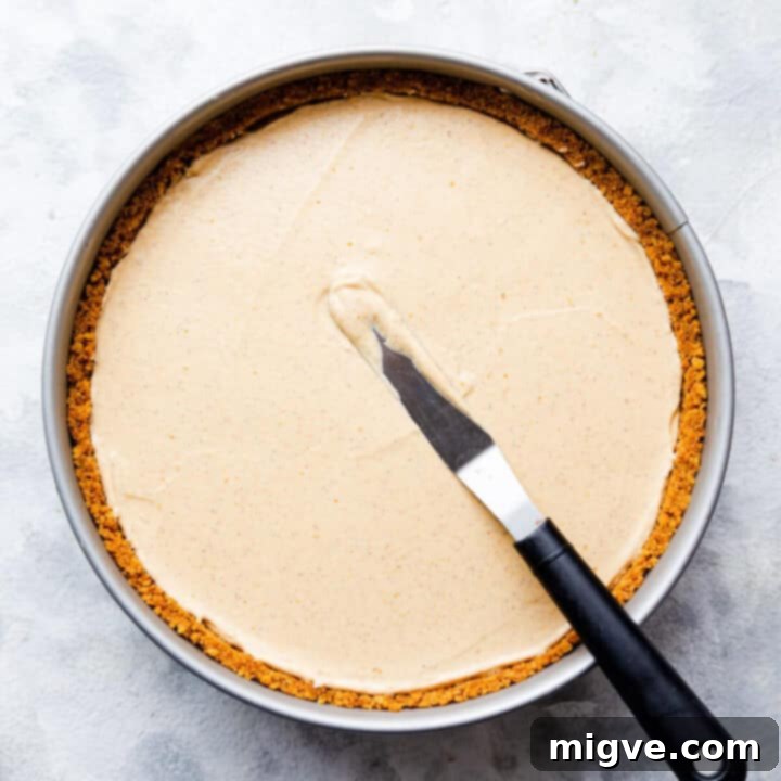 top view of a round baking tin with pumpkin cheesecake inside and small offset spatula on tiop