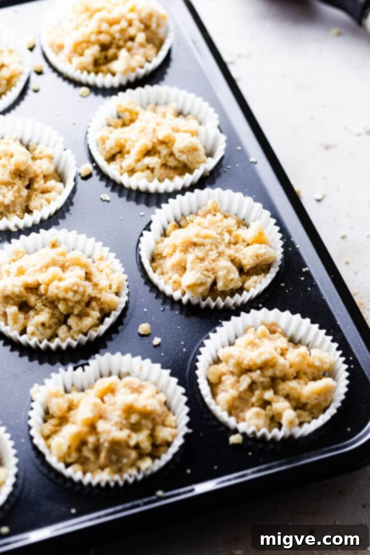 45-degree angle shot of muffin batter in paper cases in a muffin tin, generously topped with cinnamon crumble.