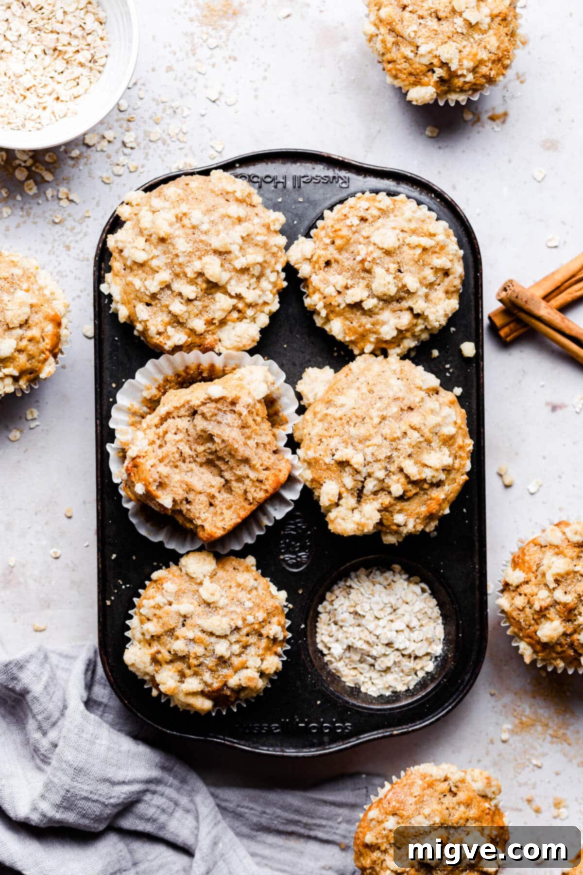 Overhead shot of 5 cinnamon oatmeal muffins in a baking tin, one with a bite missing.
