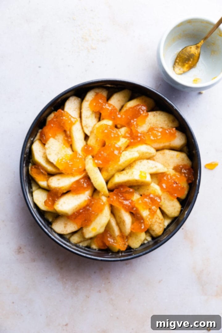 No-Fuss Apple Cake 8 overhead shot of round baking tin with sliced apples and jam on top, before the final batter layer