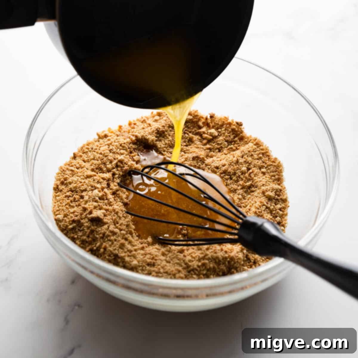 melted butter being poured into the bowl with crushed biscuits.