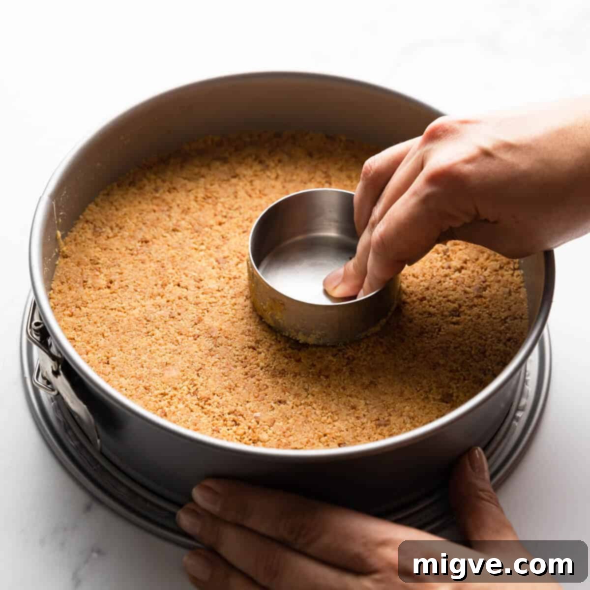 cheesecake biscuit base being pressed into the round springform baking tin.