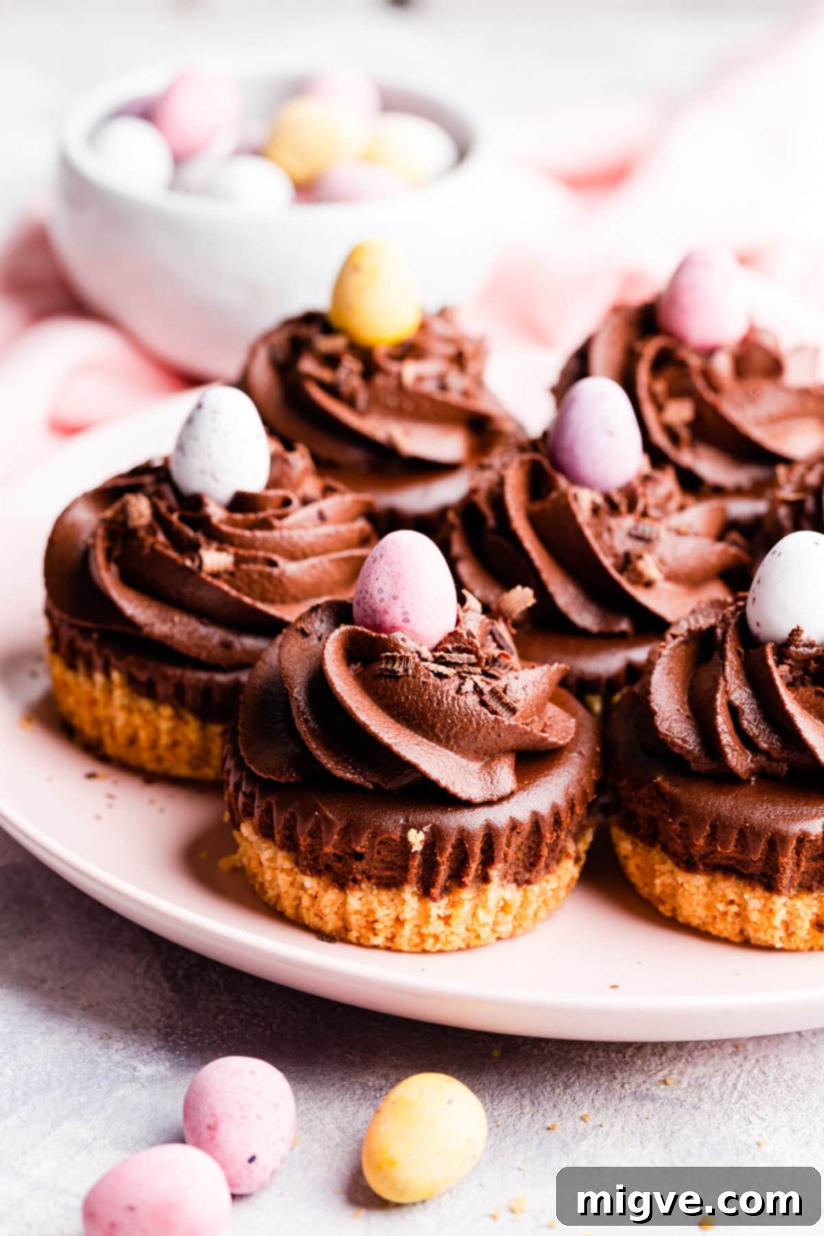 Close-up side view of individual chocolate cheesecakes on a plate, topped with whipped cream and mini chocolate eggs.