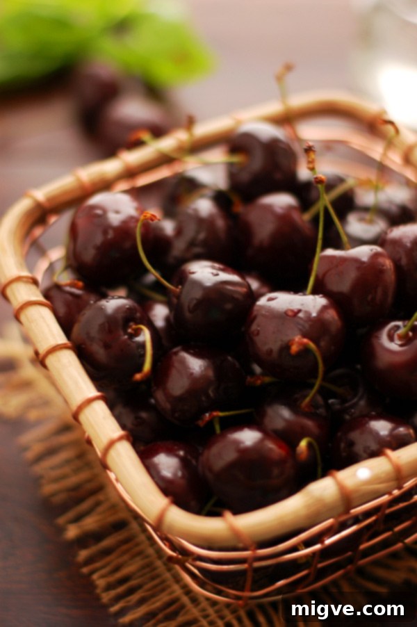Freshly made cherry and cinnamon jam in a clear glass jar, with fresh cherries scattered around.