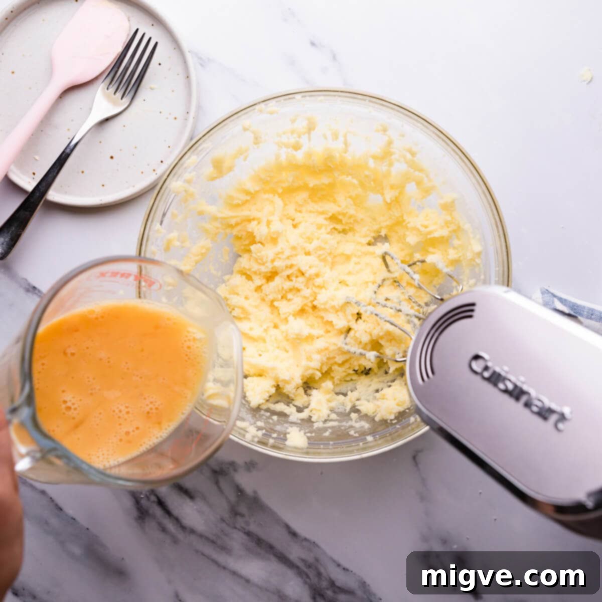 Classic Victoria Sponge 5 top view at a person adding eggs into sugar and butter mixture