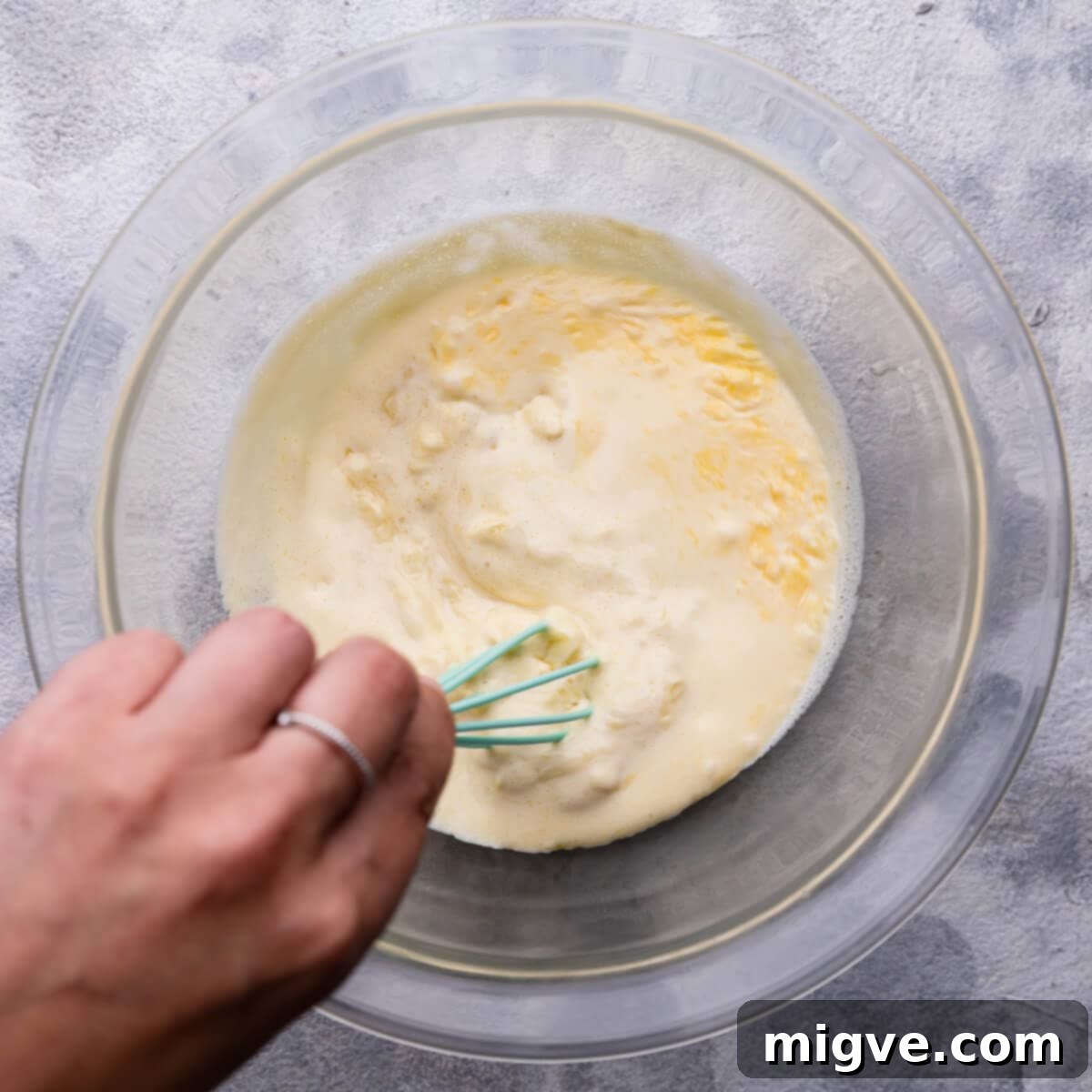 Top-down view of the white chocolate and cream mixture being gently stirred with a spatula in a bowl, transforming into a smooth, glossy ganache.