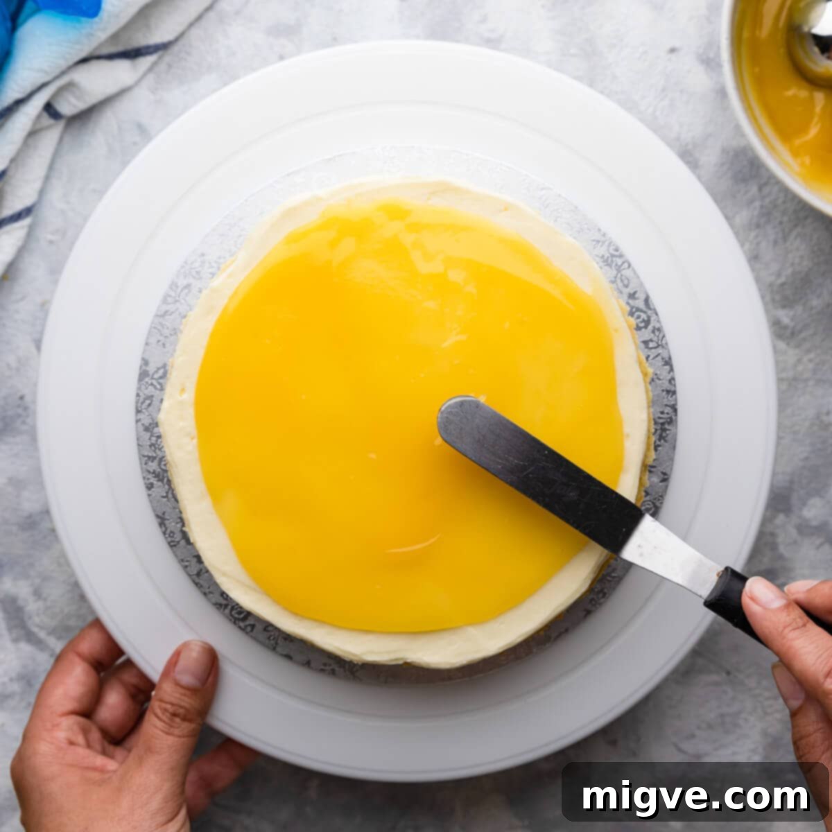 Top-down view of tangy lemon curd being gently spread over the piped elderflower buttercream layer on the cake, ensuring even distribution for a burst of flavor in every bite.