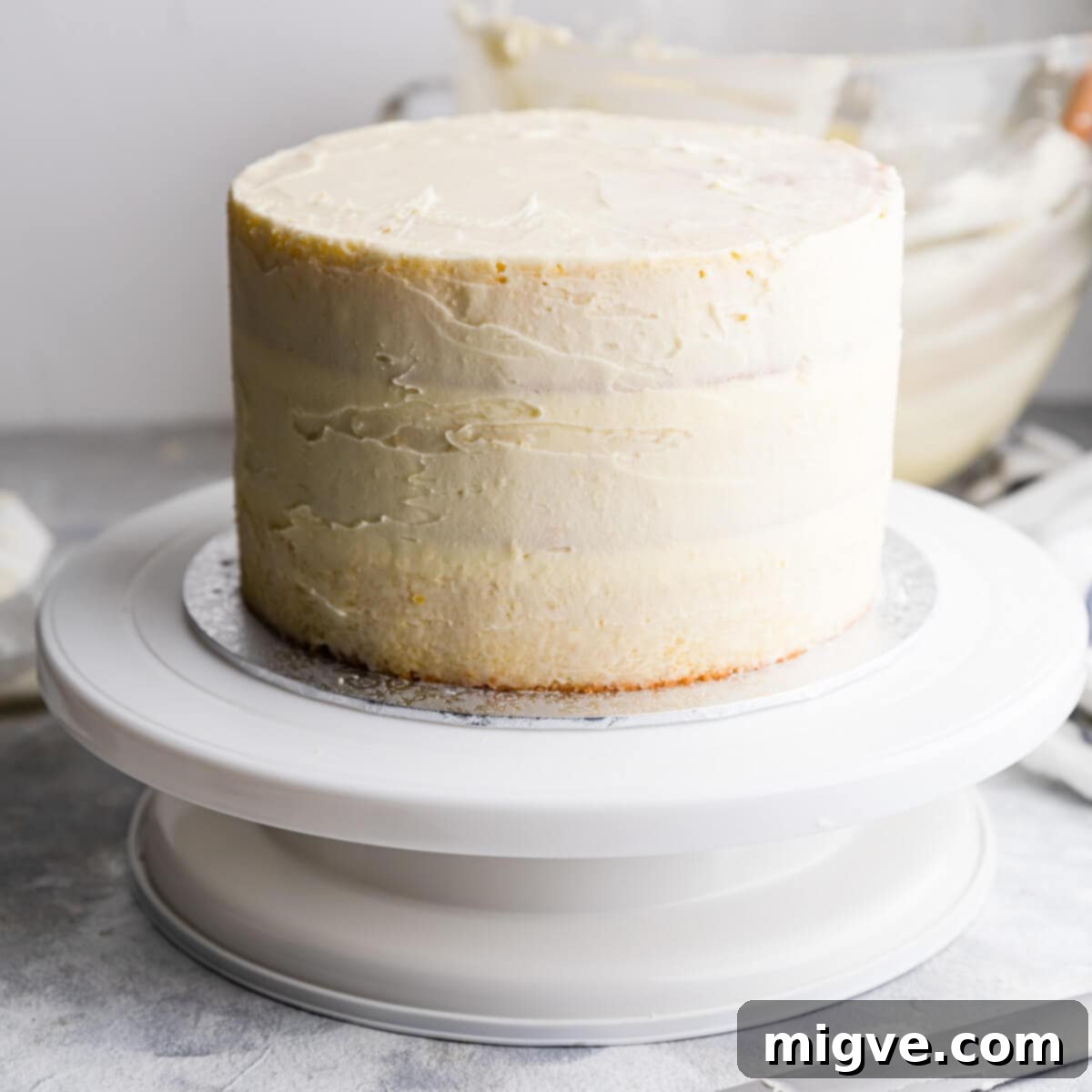 An elderflower cake with a thin, initial 'crumb coat' of icing applied to its sides and top, ready for chilling to seal in crumbs and prepare for the final frosting layer.