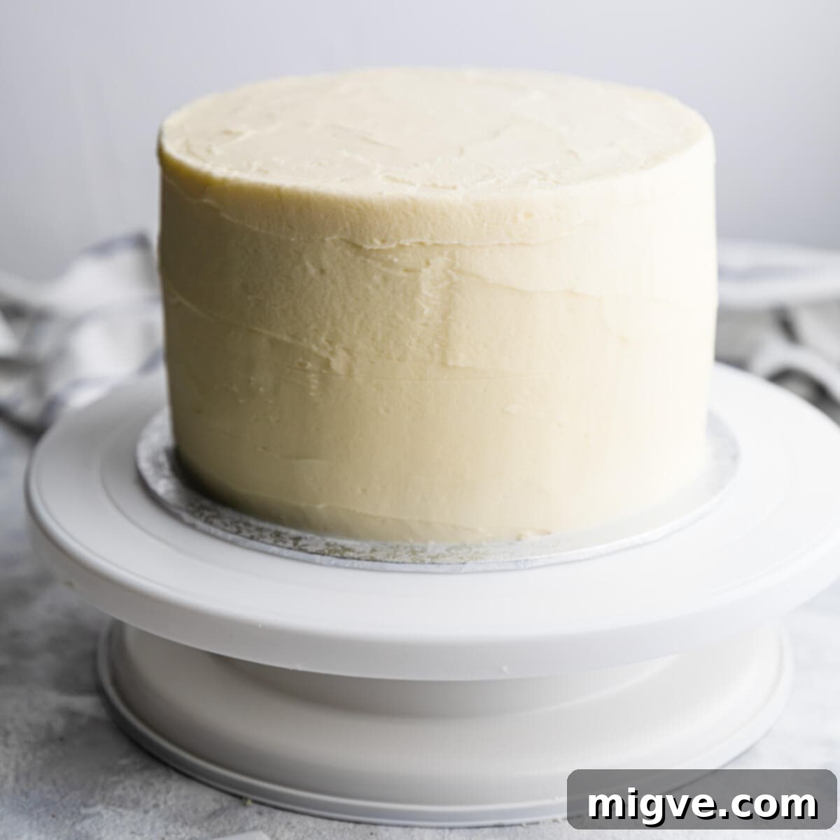 Close-up of a perfectly iced lemon and elderflower cake on a cake turntable, showcasing its smooth buttercream finish before the final drip and decorations are applied.