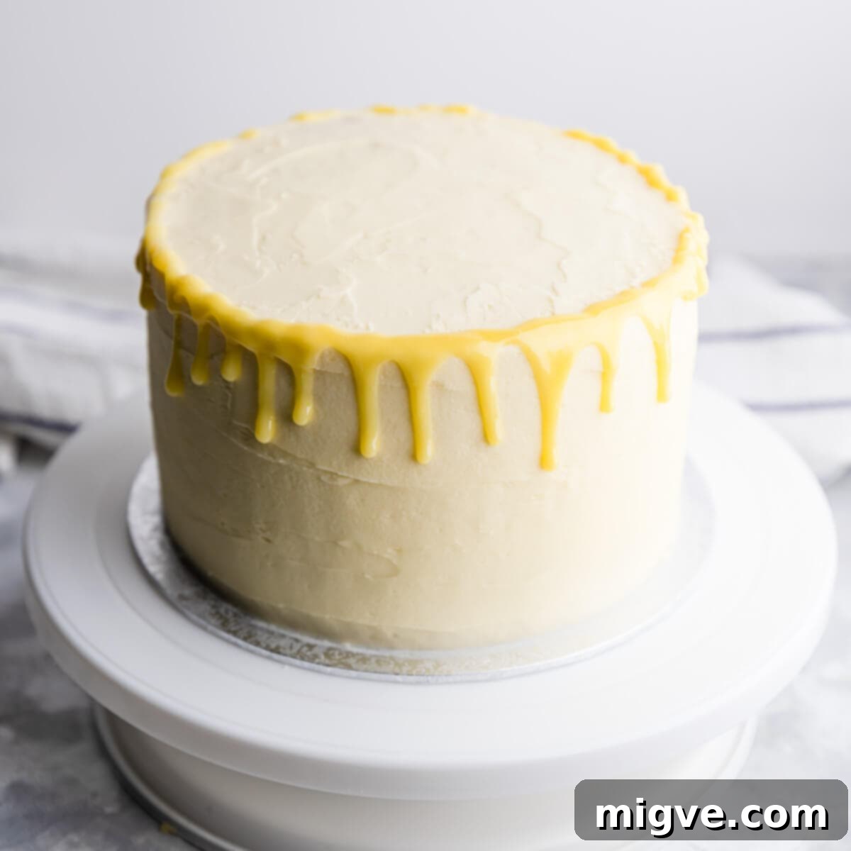 Close-up of the finished lemon and elderflower cake, featuring elegant white chocolate ganache drips flowing down the sides, topped with piped buttercream rosettes and delicate edible decorations.