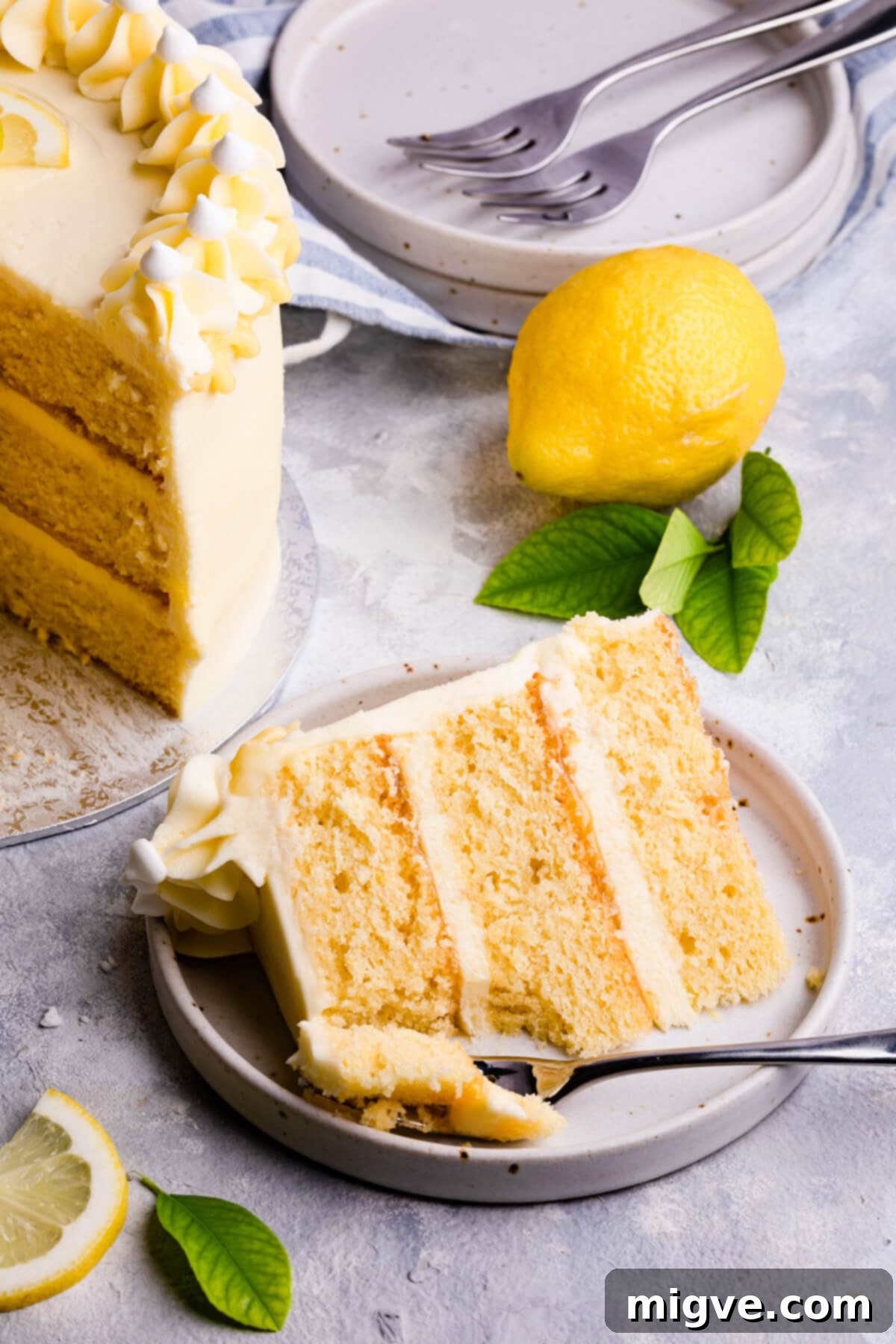 A perfectly portioned slice of elderflower and lemon cake with visible layers of sponge, buttercream, and lemon curd, sitting elegantly on a white cake plate.