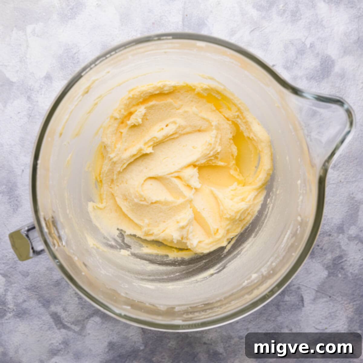 Close-up overhead view of softened butter and caster sugar creamed together in a mixing bowl until light and fluffy, showing the perfect texture for the start of the cake batter.