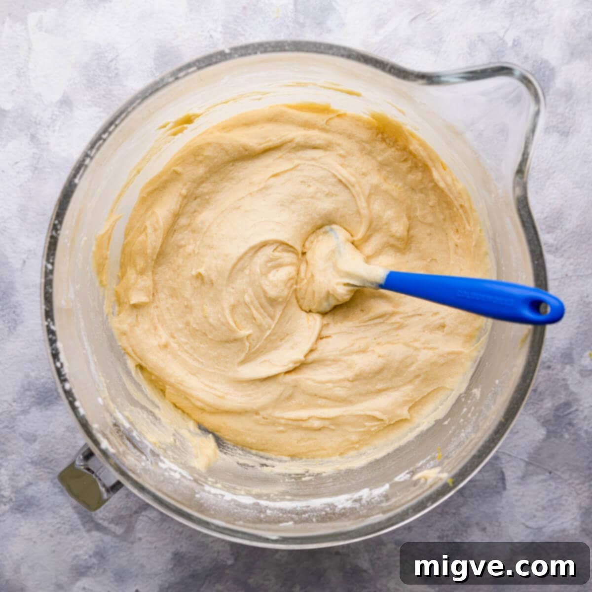 Overhead shot of a mixing bowl containing a smooth, thick cake batter, with visible flecks of lemon zest, ready to be divided into cake tins.