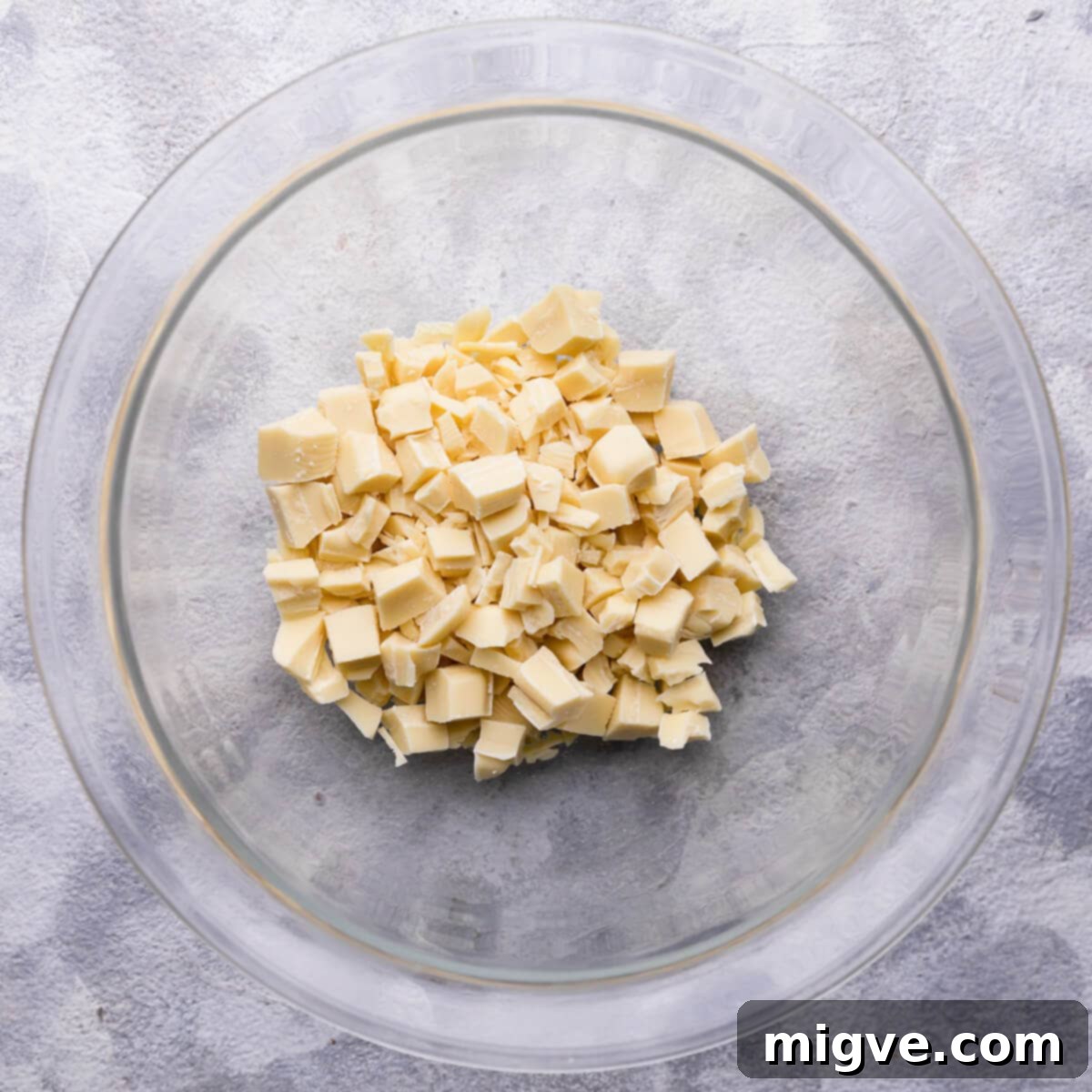 Overhead view of finely chopped high-quality white chocolate in a heatproof glass bowl, ready for ganache preparation.