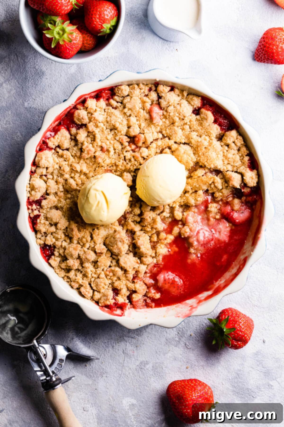 overhead view of a baked strawberry crumble with two scoops of ice cream on top