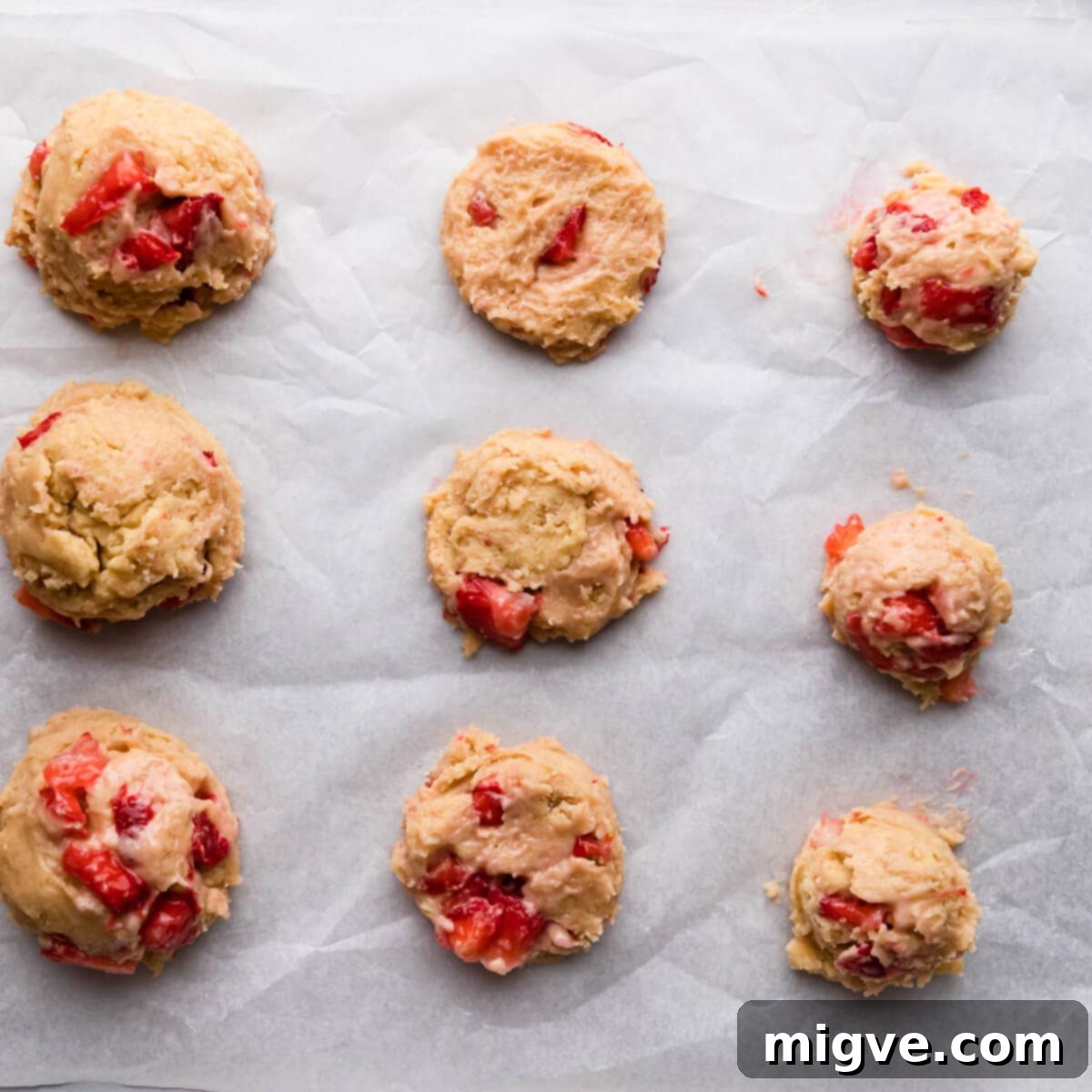 Shortcake Strawberry Cookies 7 Overhead view of scoops of cookie dough with strawberry pieces on a baking tray, with some flattened into discs.