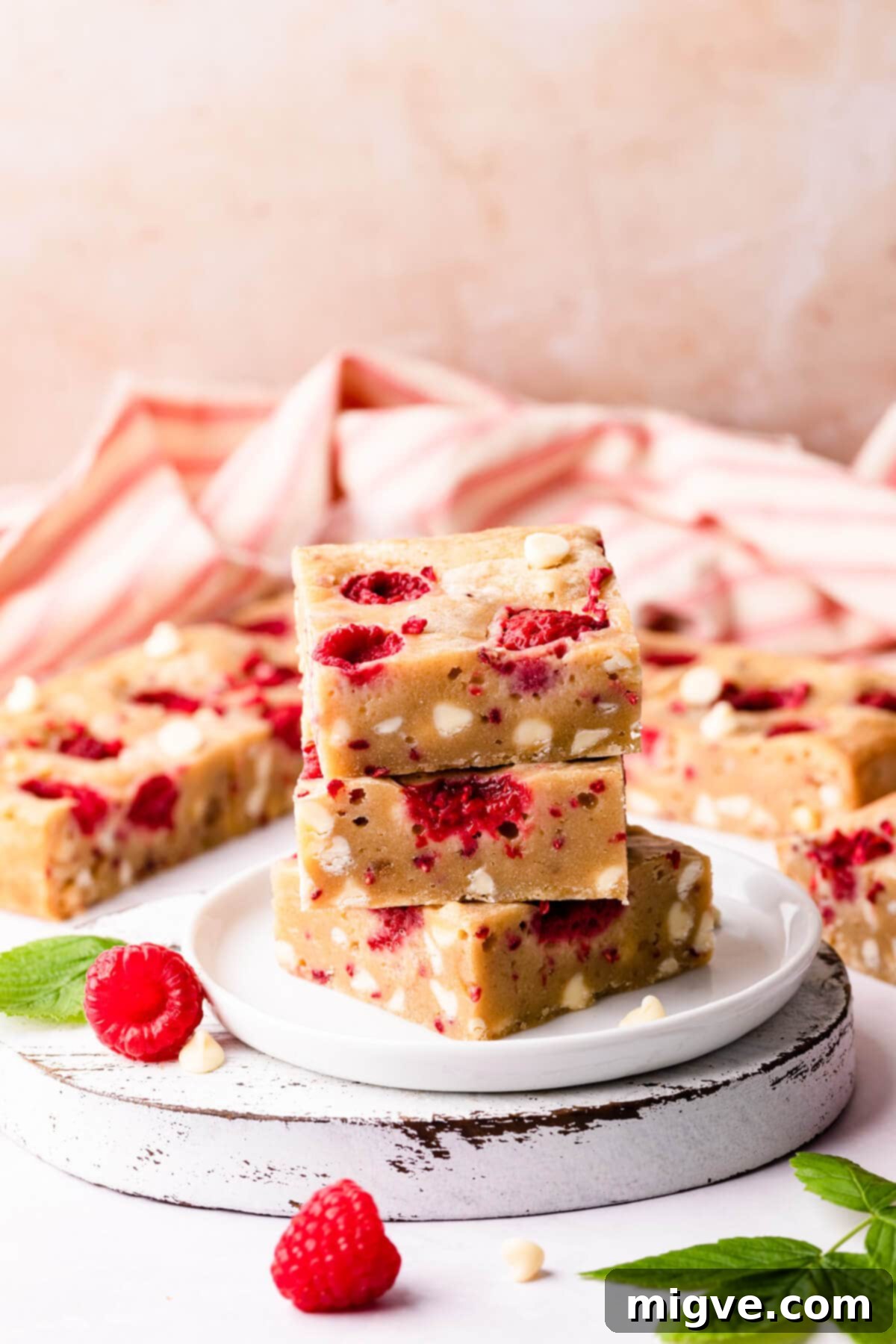 White chocolate and raspberry blondies neatly cut into squares on a small white chopping board, ready to be served.