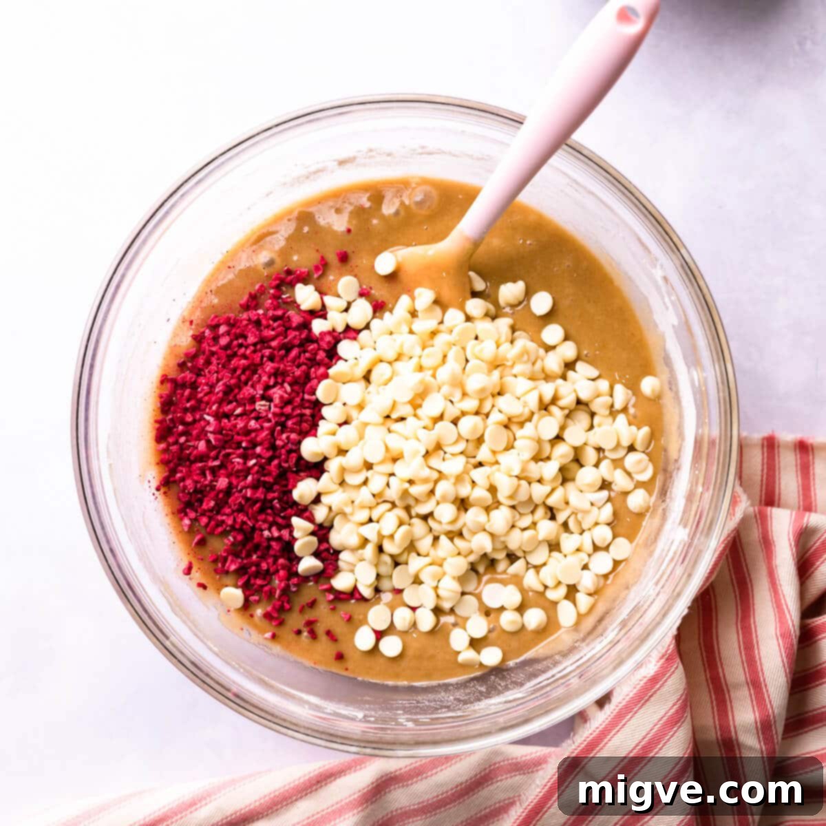 Blondie batter in a bowl with white chocolate chips and freeze-dried raspberries added, ready for the final mix.