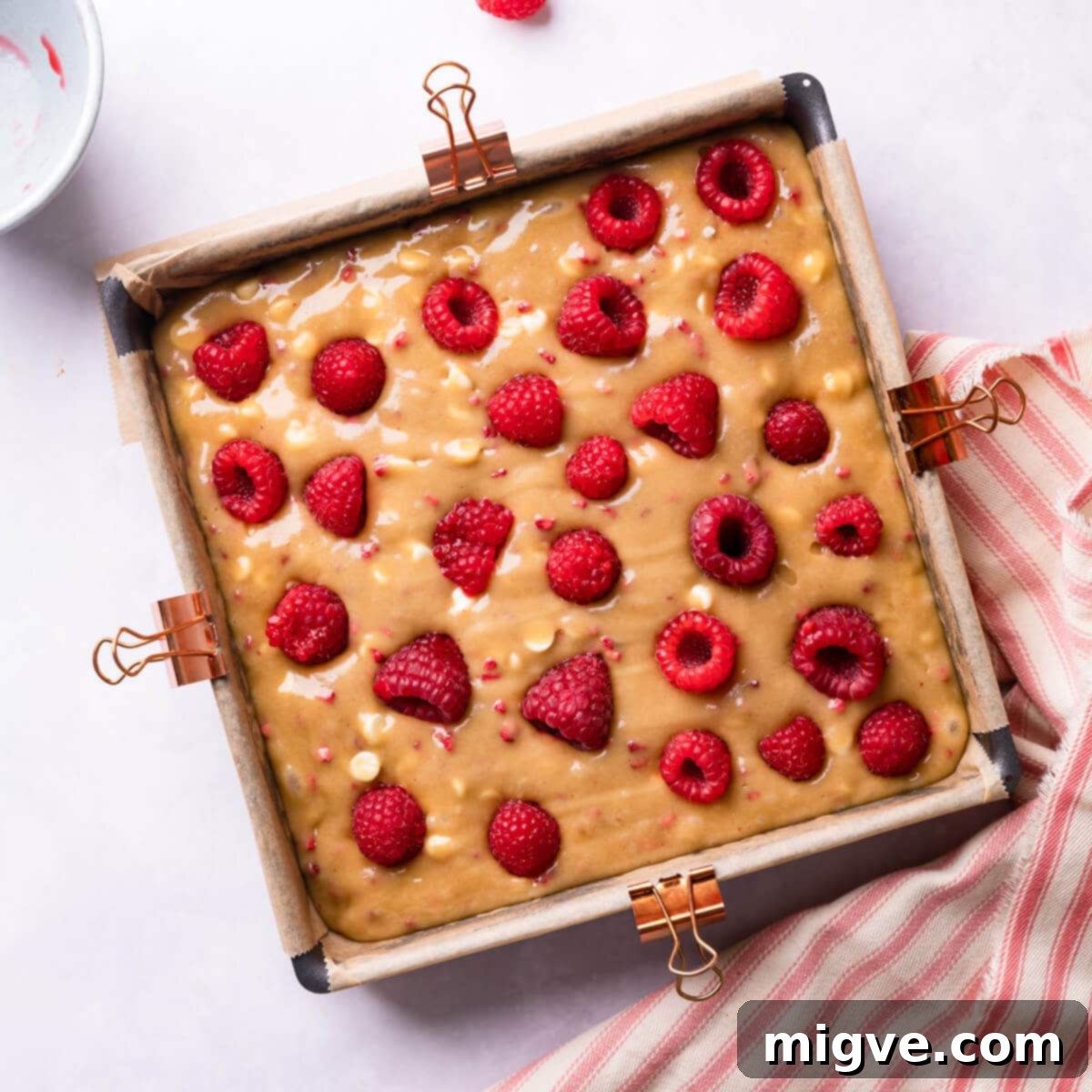 A baking tin filled with blondie batter, topped with fresh raspberries before baking.