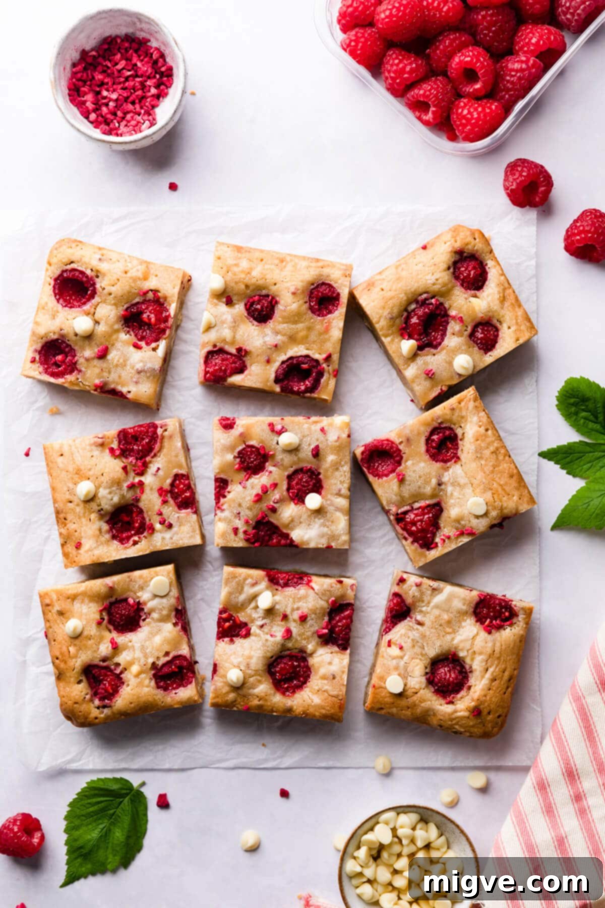 Nine square slices of beautifully baked blondie bars, featuring raspberries and white chocolate, arranged on a clean white surface.