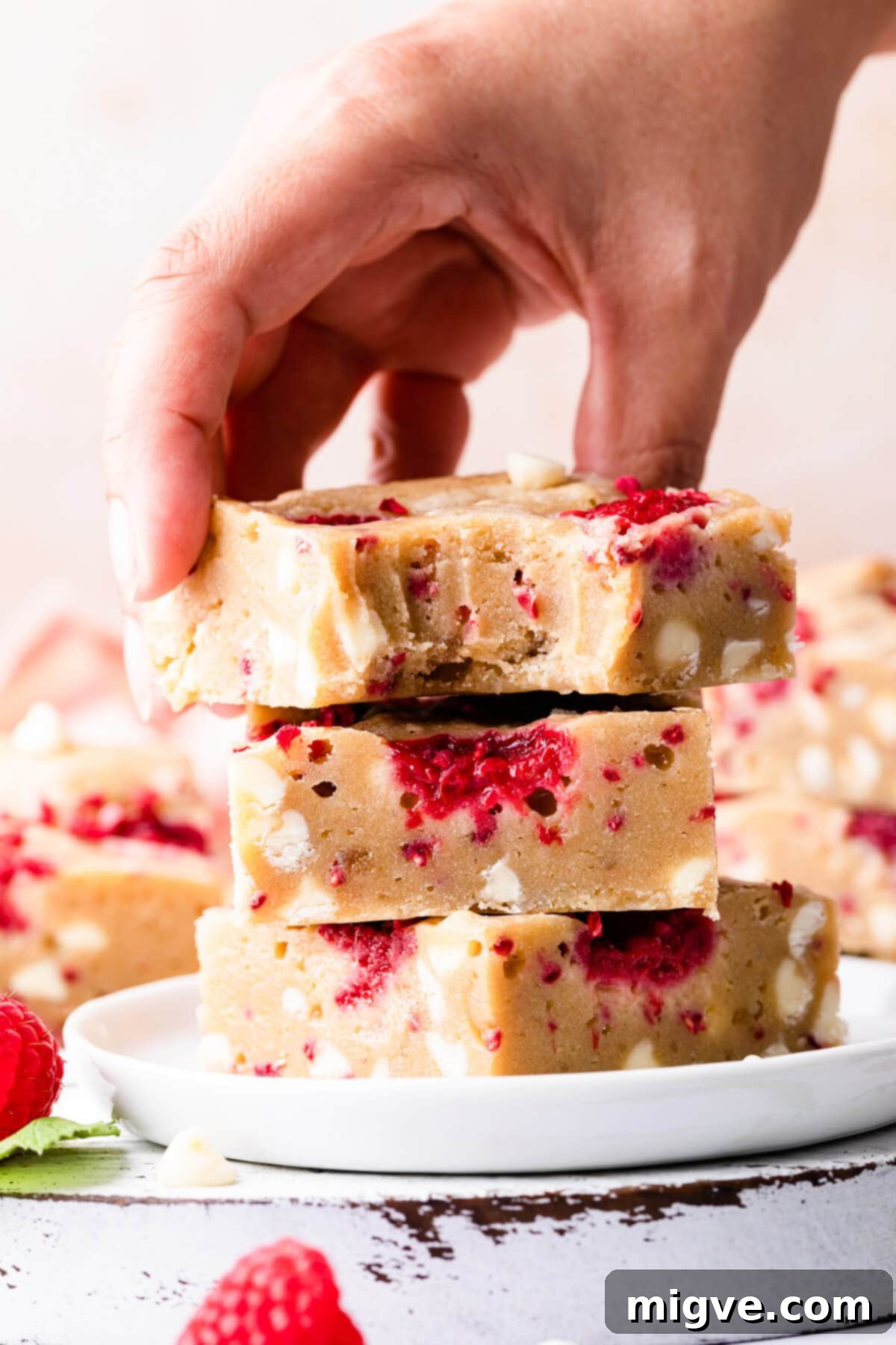 Three decadent blondie bars stacked on top of each other, with a hand reaching for the top one, showcasing their irresistible texture.
