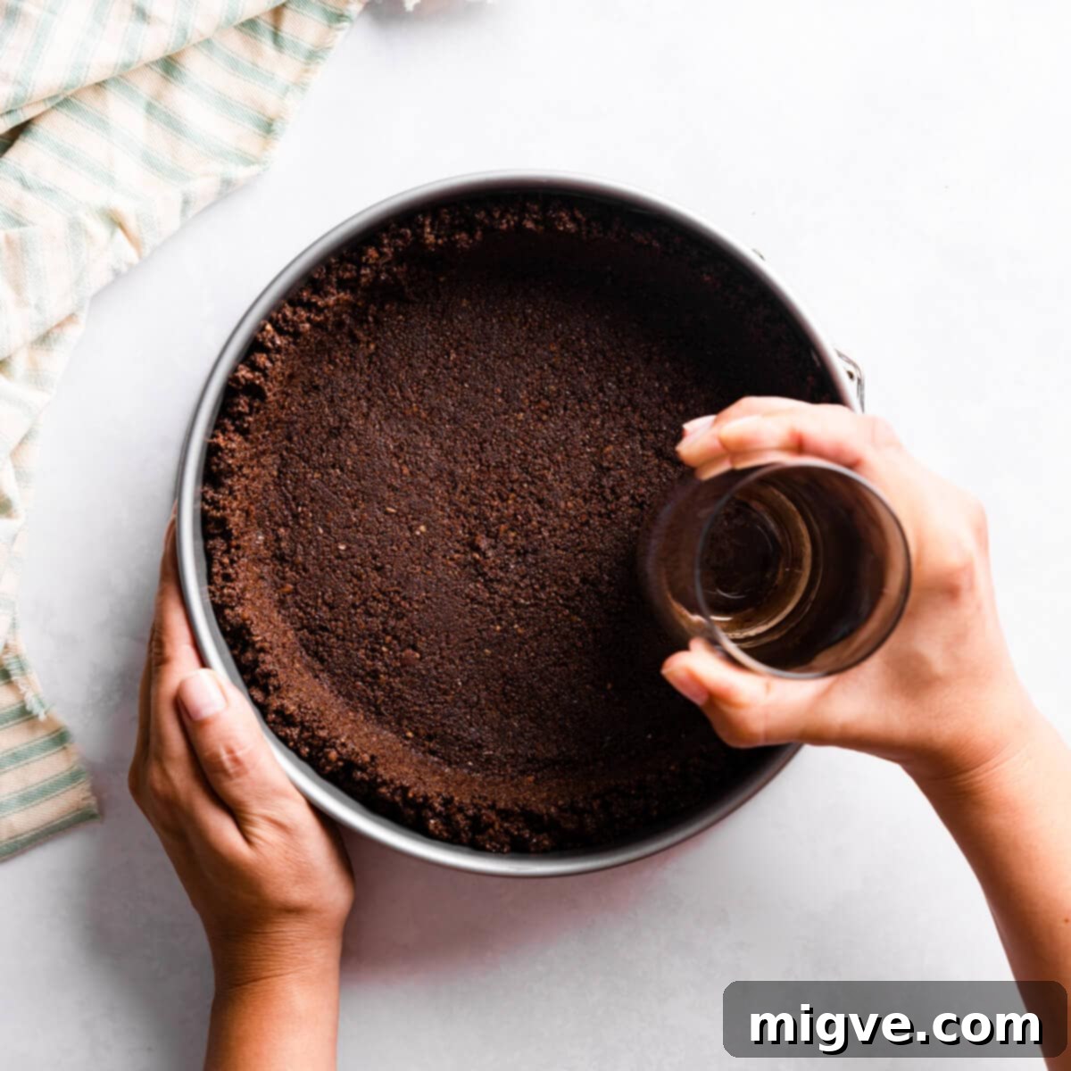 Sinfully Decadent Cheesecake 4 cheesecake crust being pushed into baking tin with a glass.
