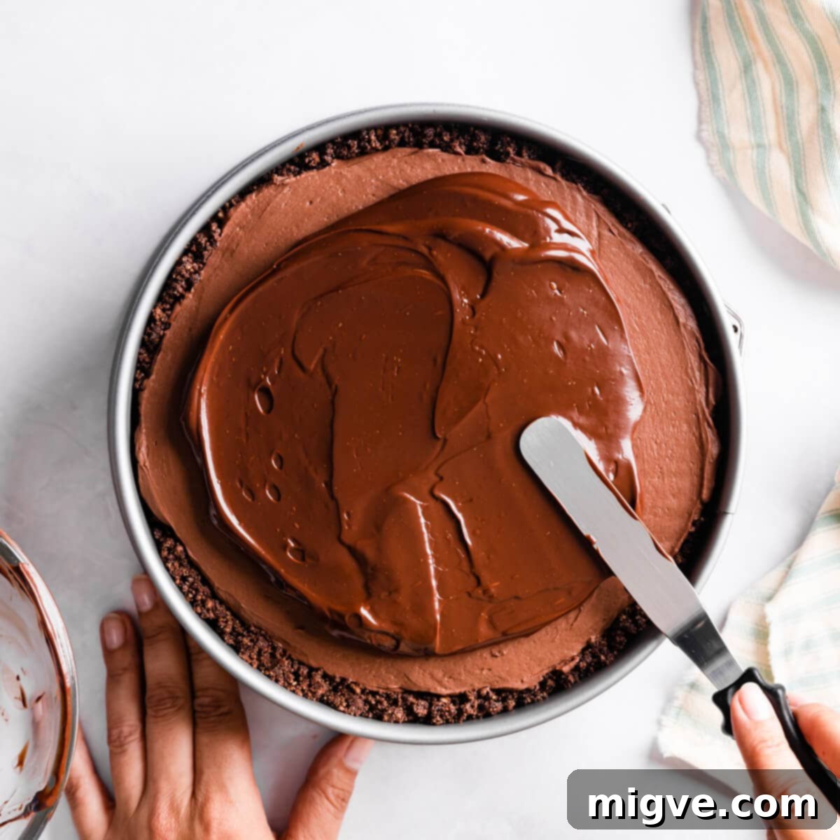 Sinfully Decadent Cheesecake 7 chocolate ganache being spread on top of the cheesecake with offset spatula.