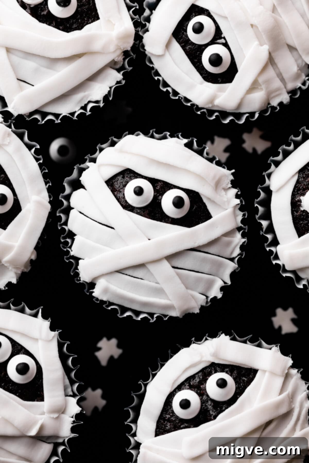 Bandaged Boo Cupcakes 2 Delightful Halloween mummy cupcakes with white icing and expressive candy eyes, sitting on a dark background, ready for a spooky season party. Soft and moist chocolate cupcake topped with decorative icing and sugar eyes.