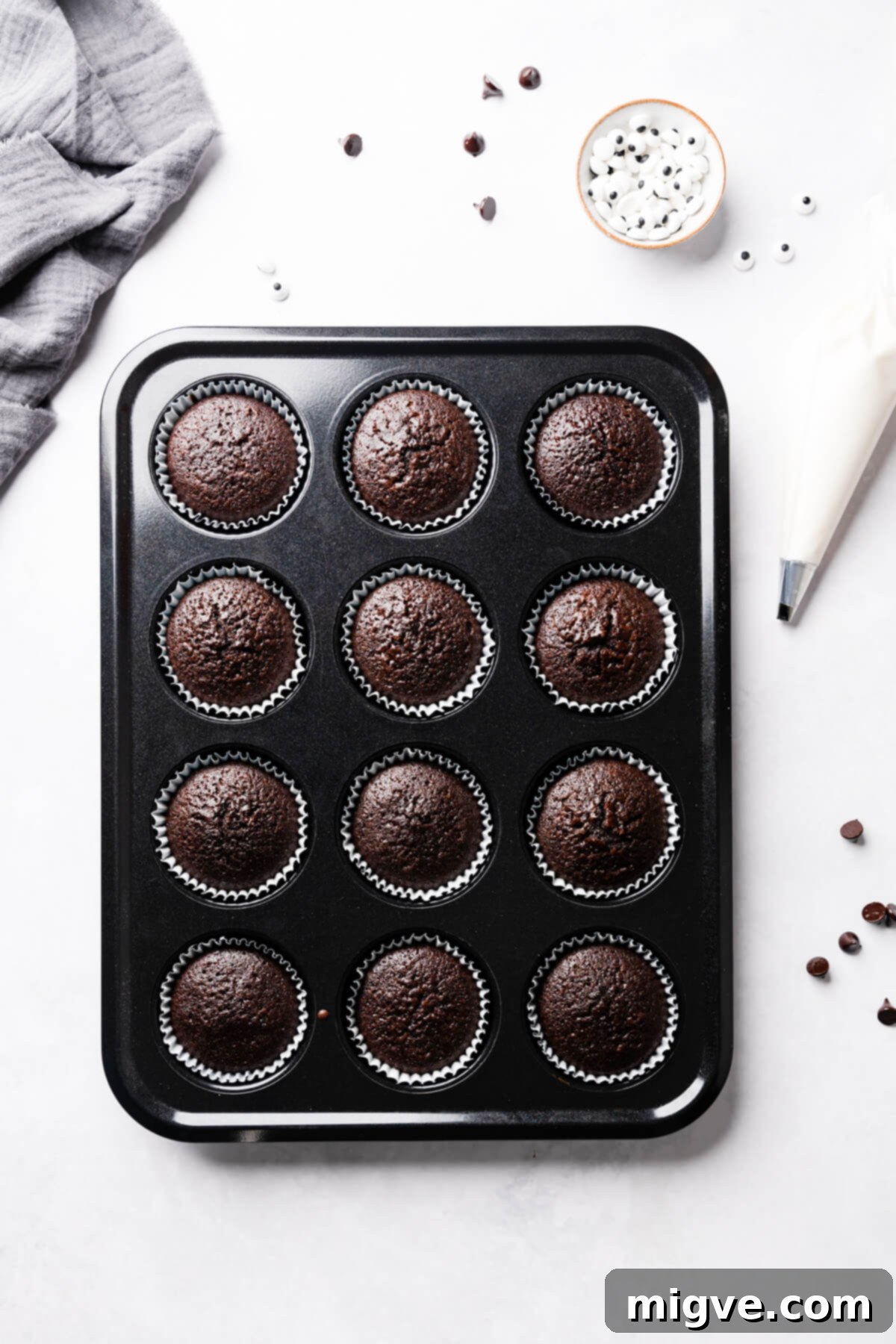 Bandaged Boo Cupcakes 8 Freshly baked chocolate cupcakes cooled in their baking tin, surrounded by sugar eyes and chocolate chips, awaiting decoration.