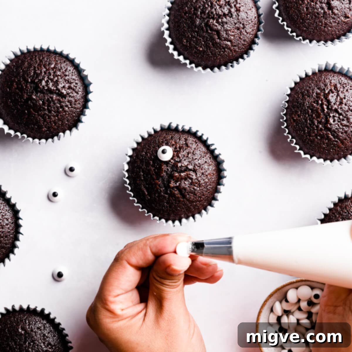 Bandaged Boo Cupcakes 9 A small dollop of icing being applied to the back of a sugar eye before carefully sticking it onto a chocolate cupcake.