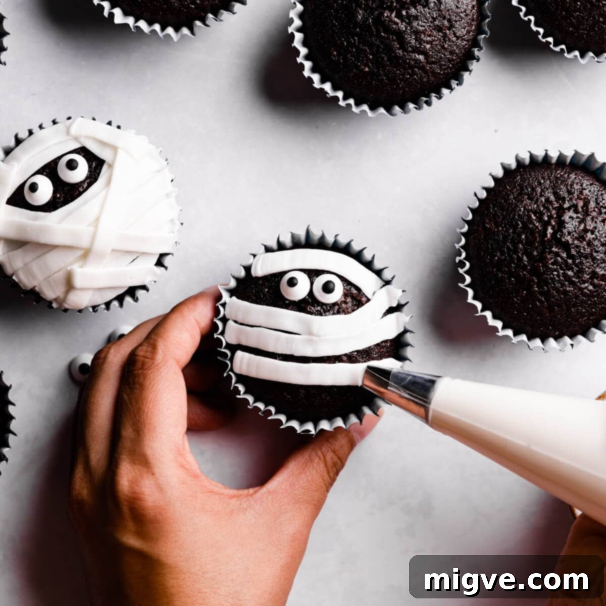 Bandaged Boo Cupcakes 10 White royal icing being piped in straight and uneven lines across the top of a cupcake, creating a mummy bandage effect, leaving the candy eyes visible.