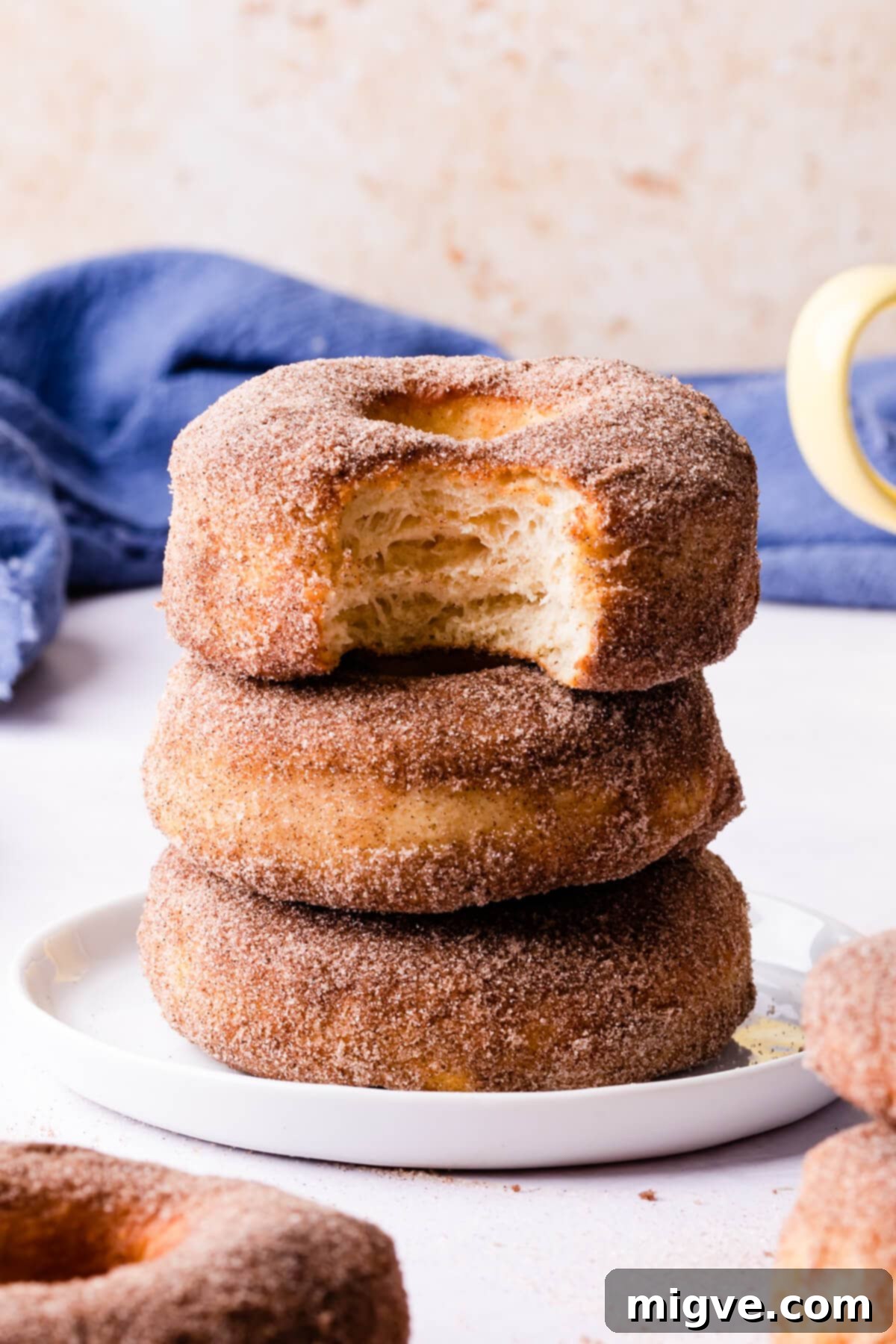 A beautifully arranged stack of air-fried doughnuts on a small white plate, with the top doughnut having a bite taken out, revealing its soft, airy interior.