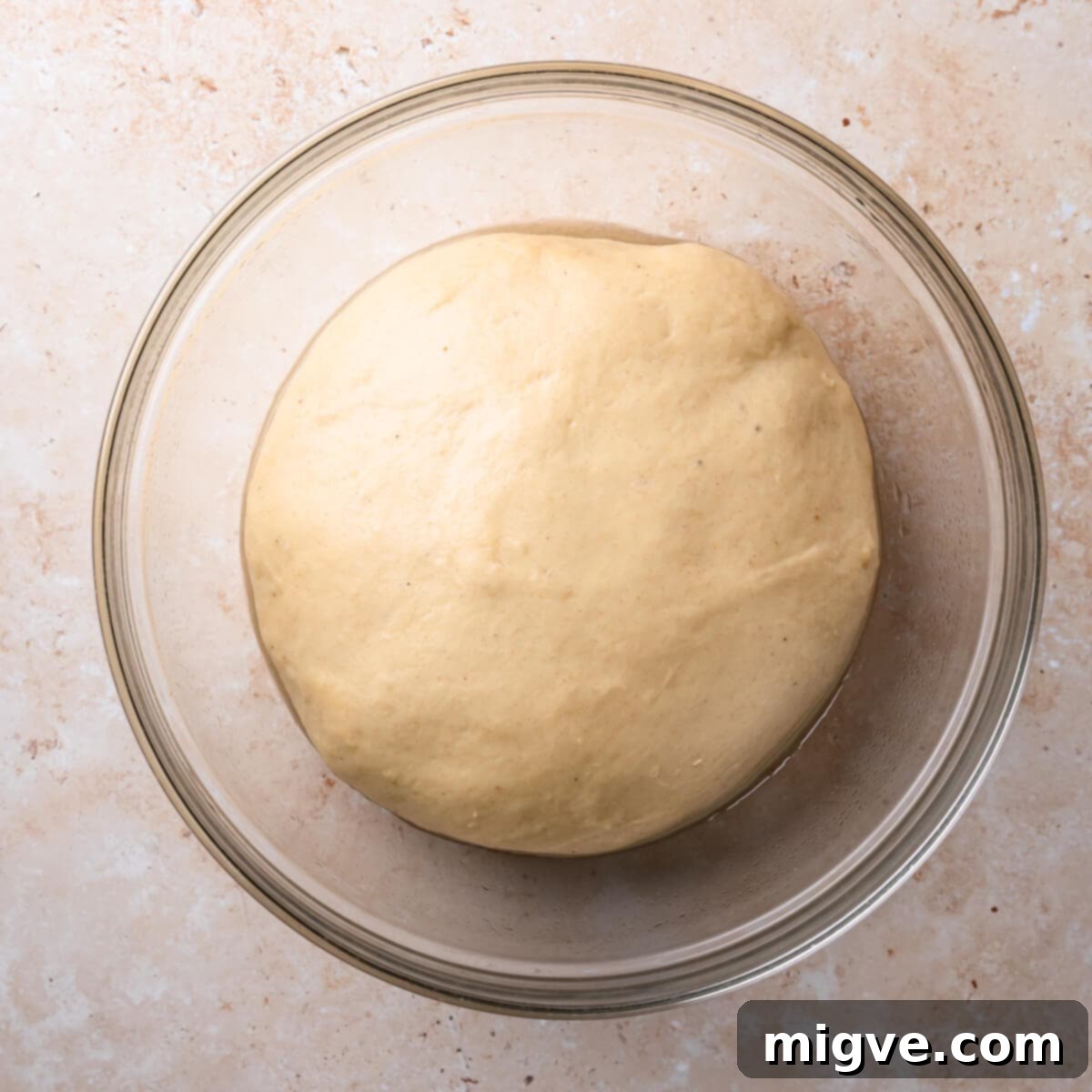 Well-proofed yeasted dough, visibly doubled in size, in a glass bowl, indicating readiness for shaping.