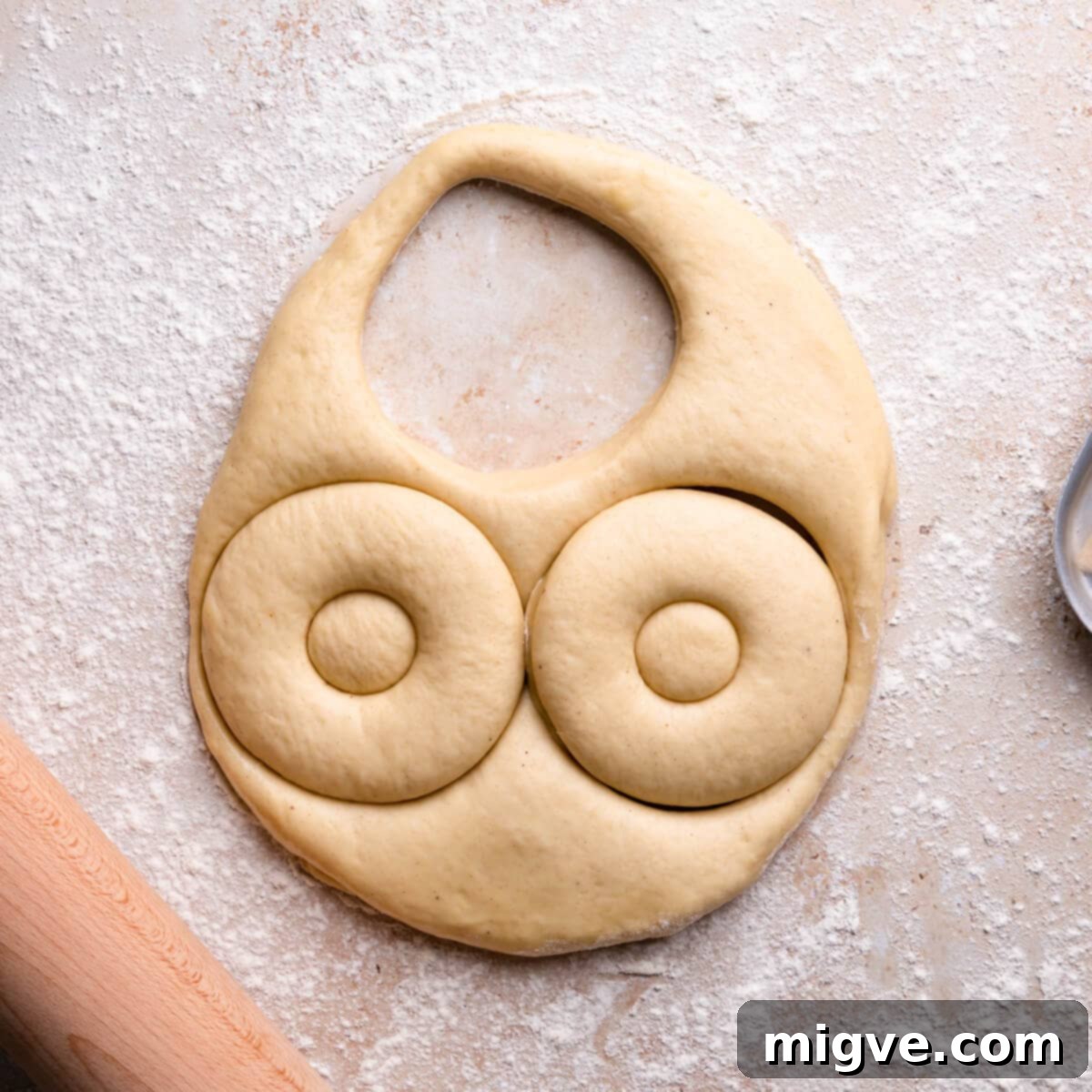 Doughnut shapes being carefully cut from the risen dough using a doughnut cutter.