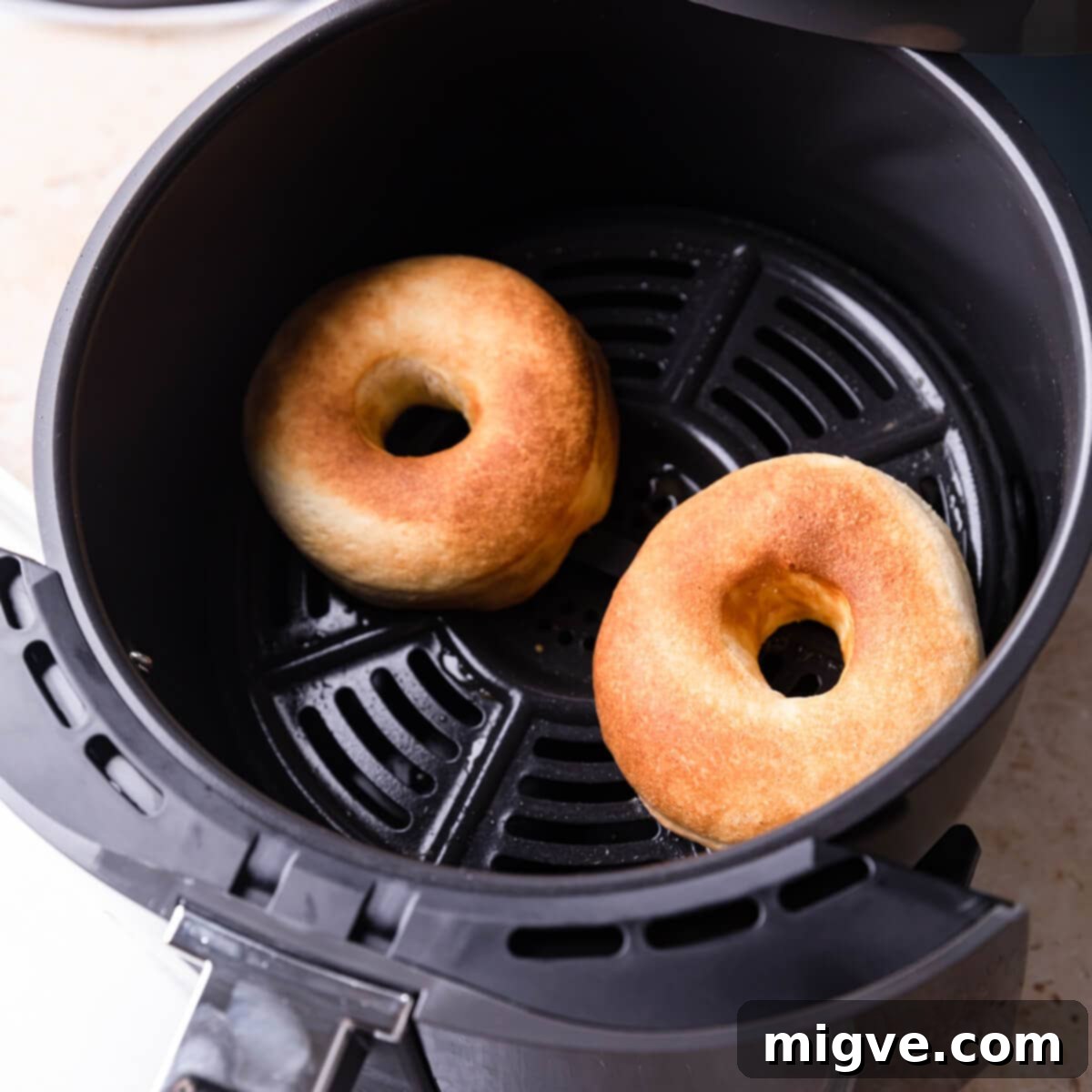 Two unglazed doughnuts placed carefully in the basket of an air fryer, ready for cooking.