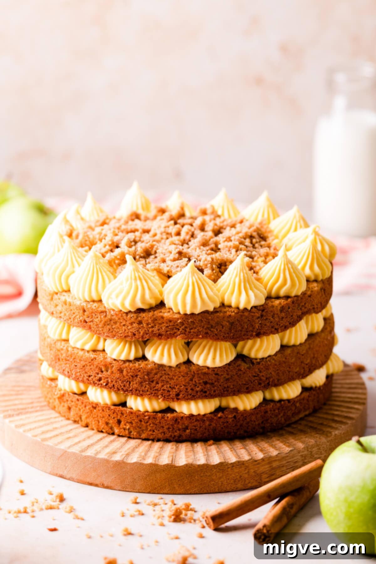 apple cake on a wooden cake stand with cinnamon sticks on side.
