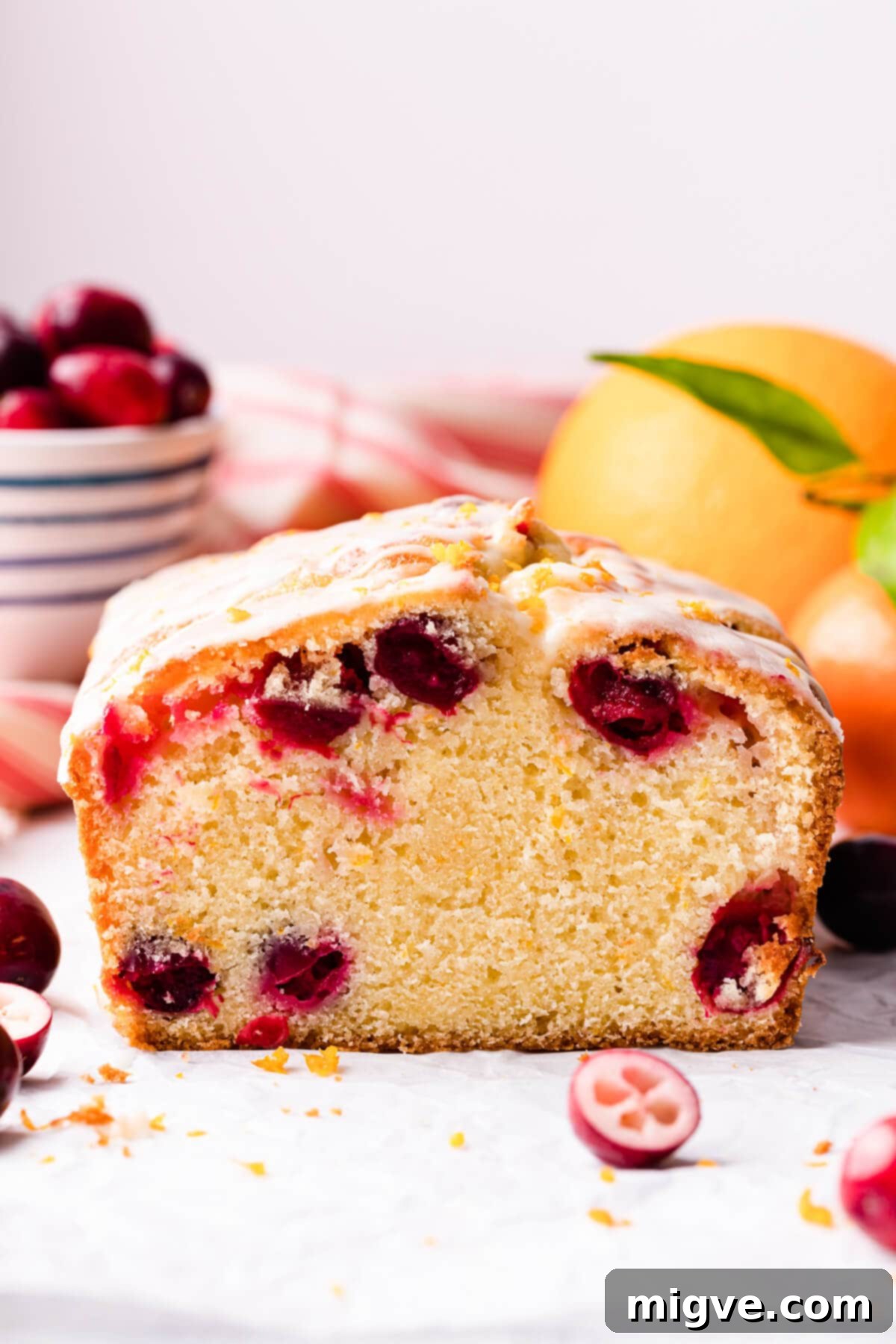 orange cranberry loaf on a white surface and some fresh cranberries around it.